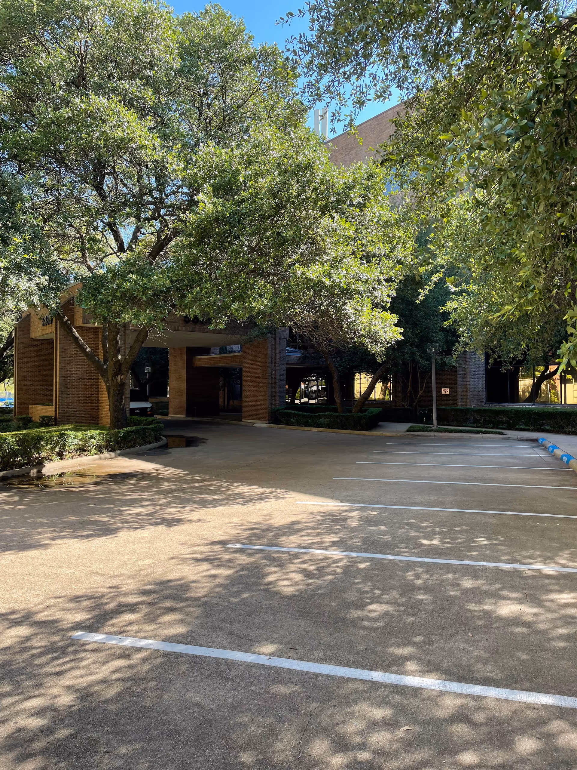 Tree-shaded parking lot in front of a brick senior living facility entrance.