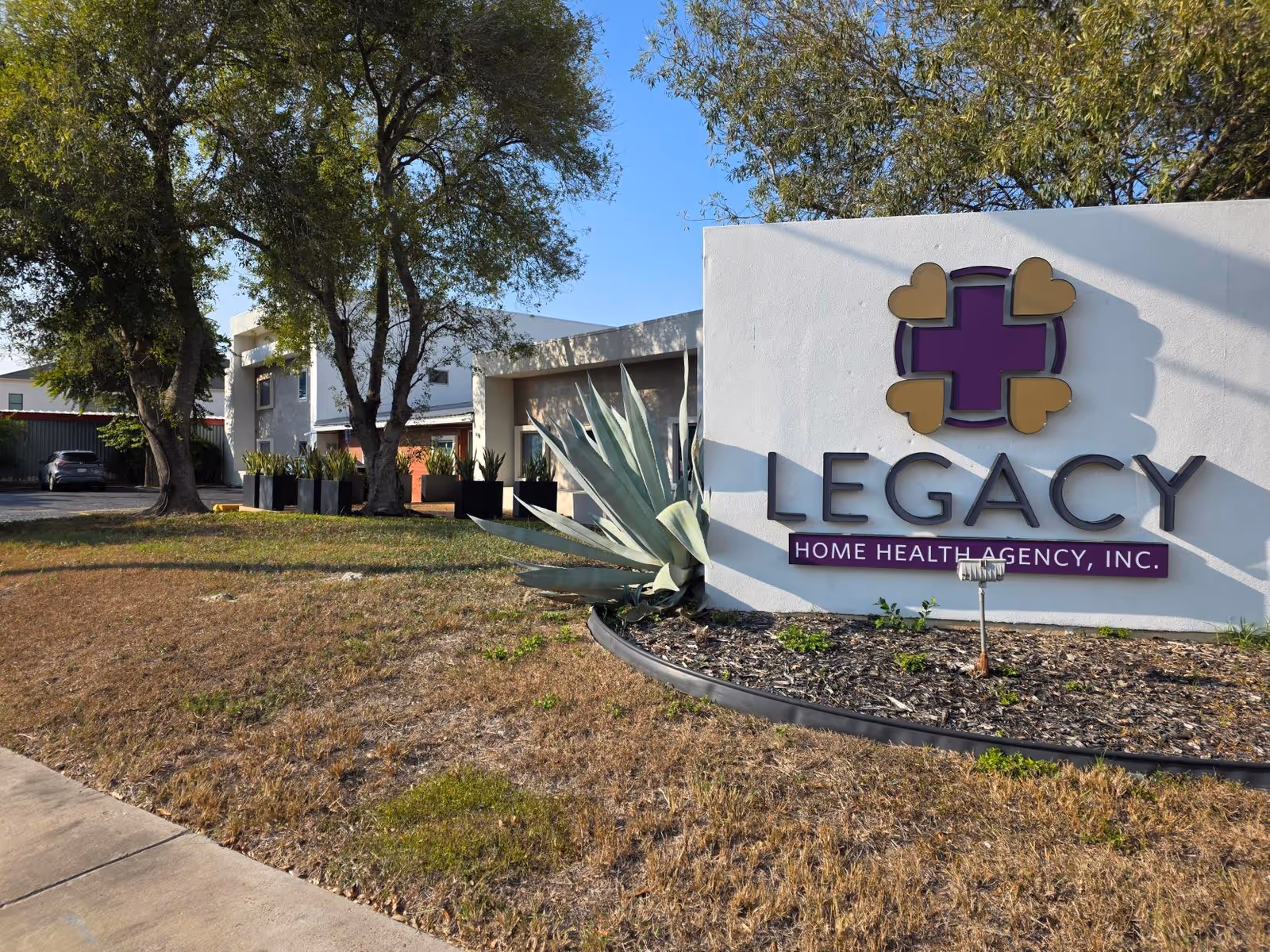 Front exterior of Legacy Home Health Agency sign with landscaping and trees.