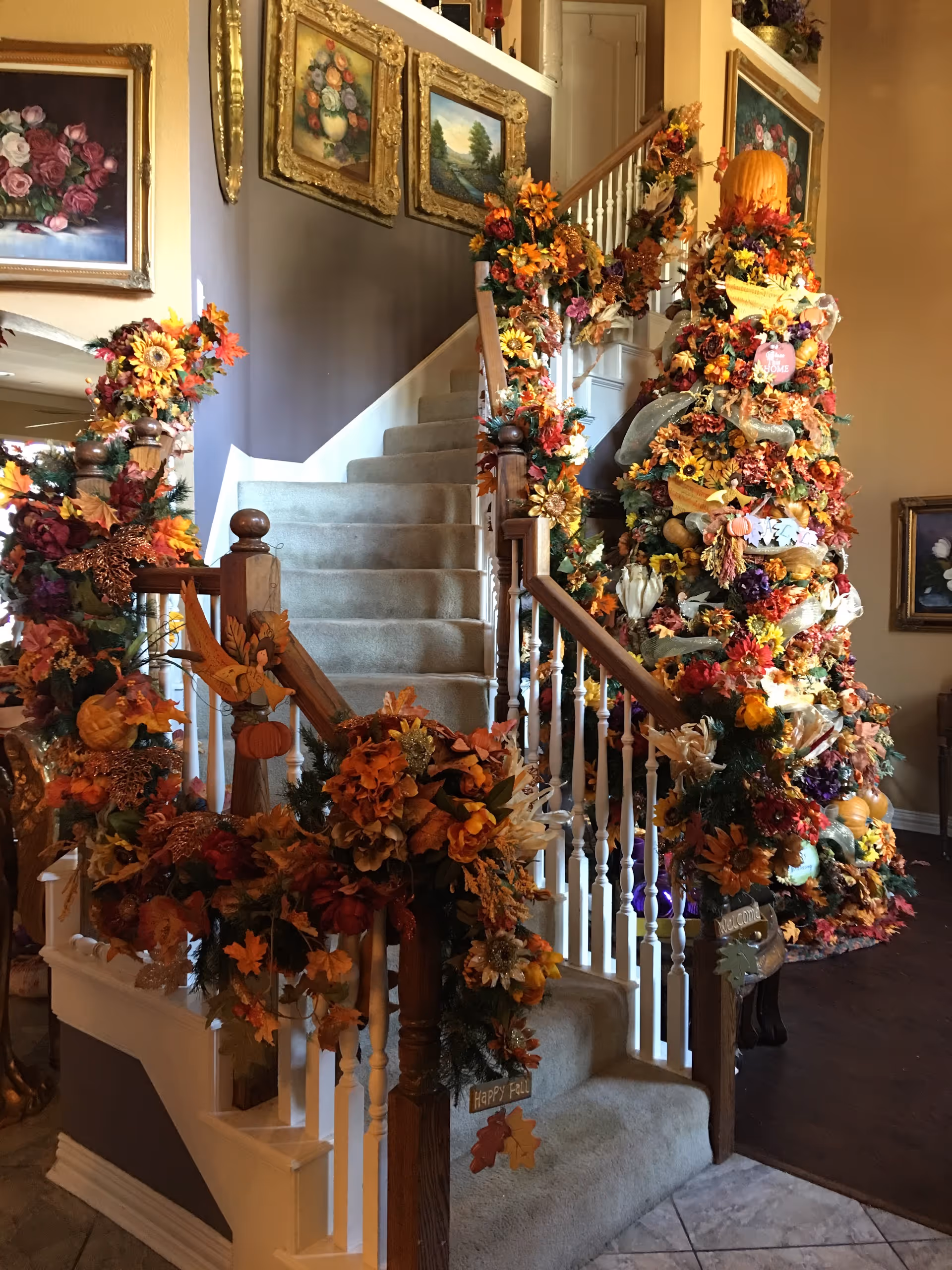 Carpeted staircase and banister lavishly decorated with autumn flowers, pumpkins, and fall-themed ornaments inside the facility.