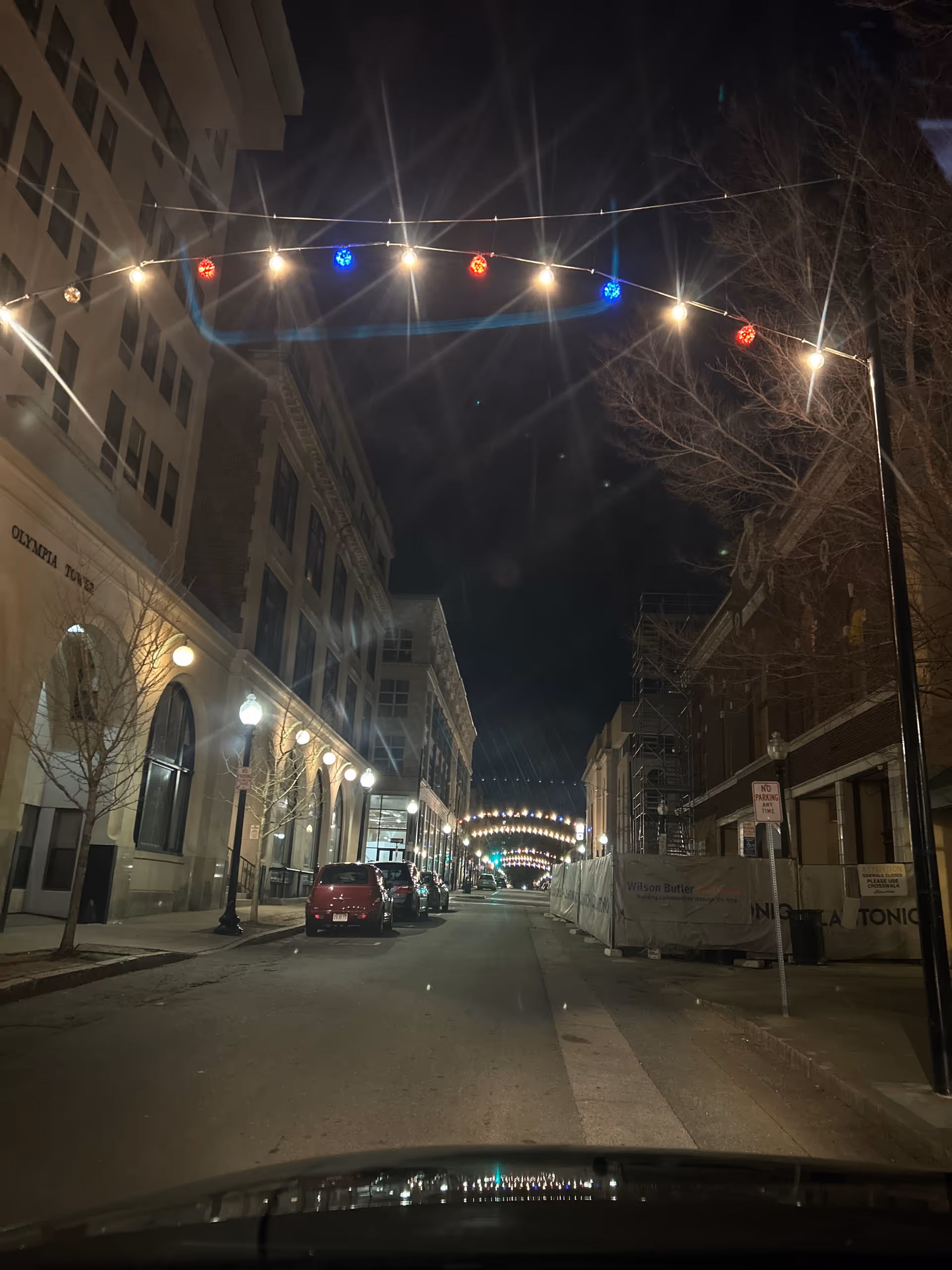 Nighttime street scene with string lights, lit storefronts, and ongoing construction along a city block.