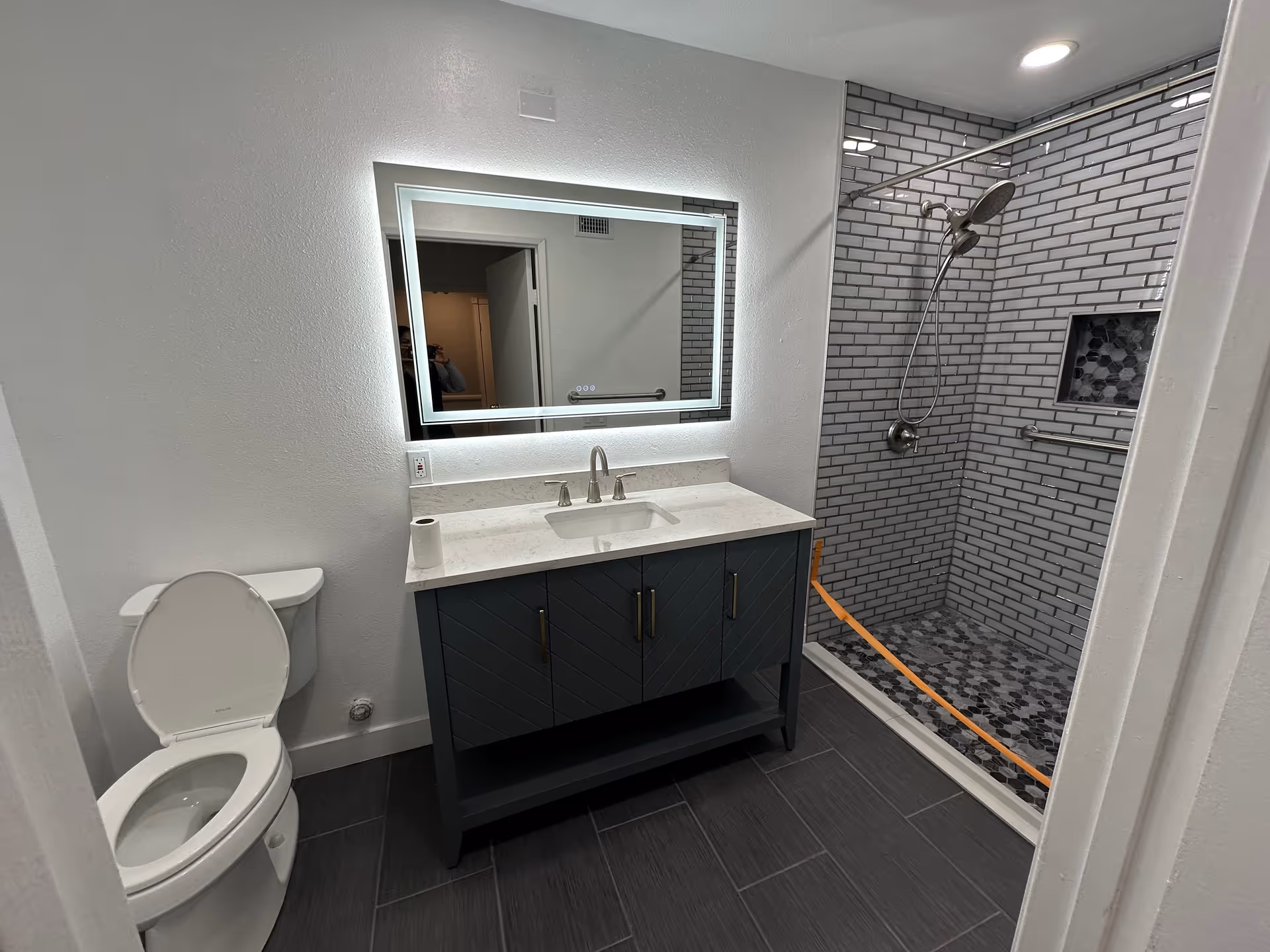 Bright bathroom with a toilet, vanity, illuminated mirror, and walk-in tiled shower.