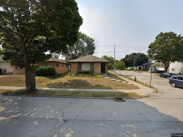 Single-story brick house with a front lawn and sidewalk on a quiet residential street.
