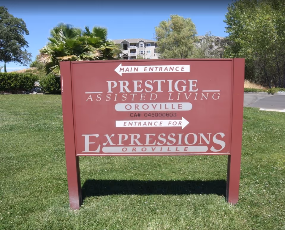 Red roadside sign on a grassy lawn that reads 'Prestige Assisted Living Oroville' with arrows to the entrance.