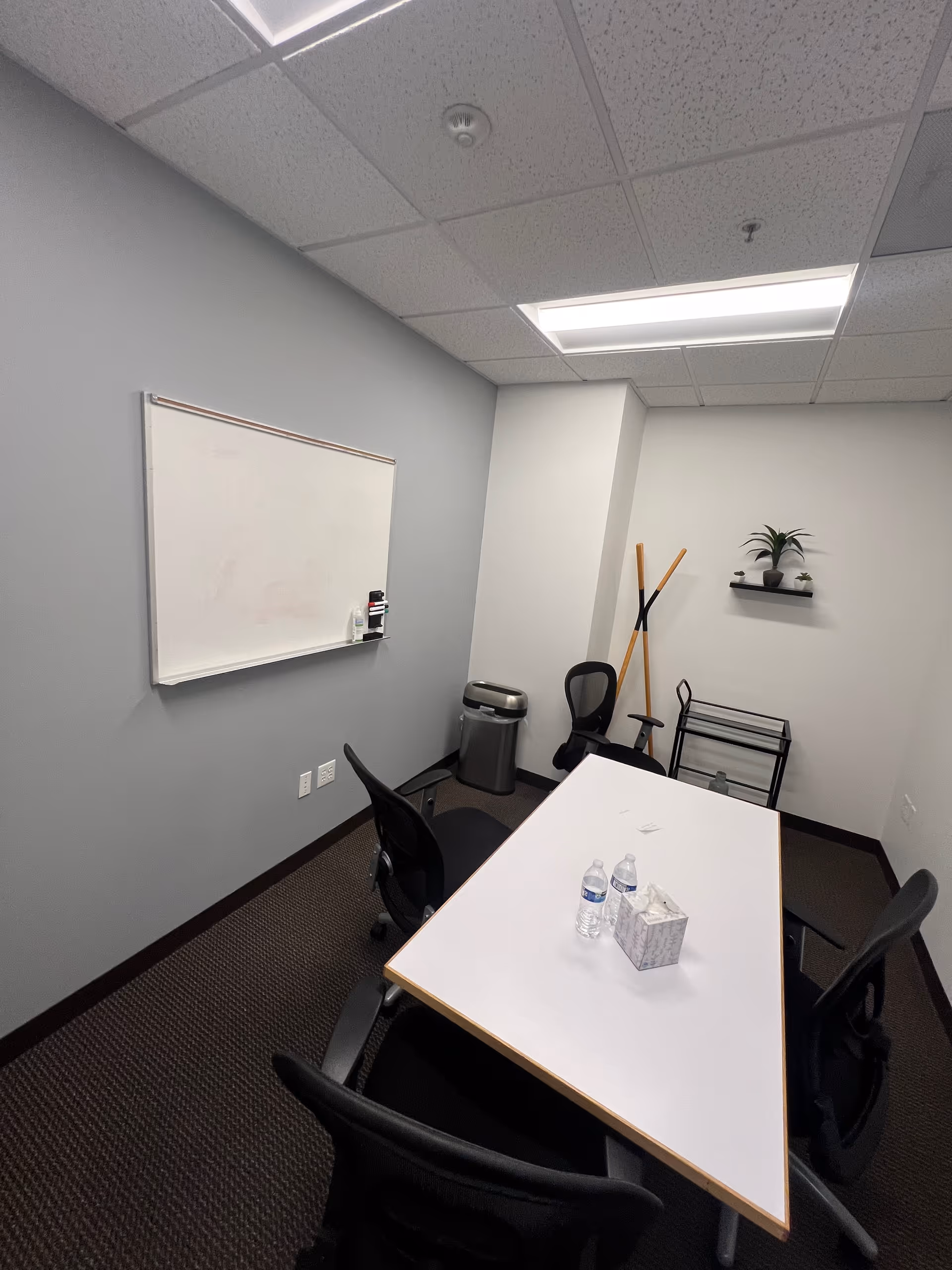 A small conference room with a whiteboard, table, chairs, water bottles, and decor.