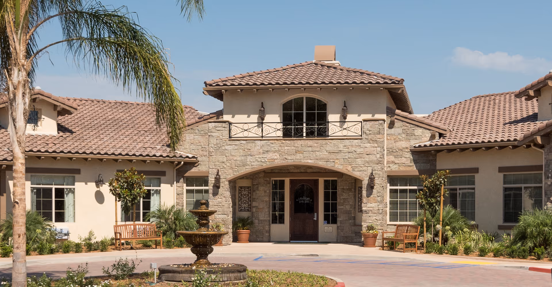 Front entrance of ActivCare at Yorba Linda featuring stone facade, fountain, and benches.