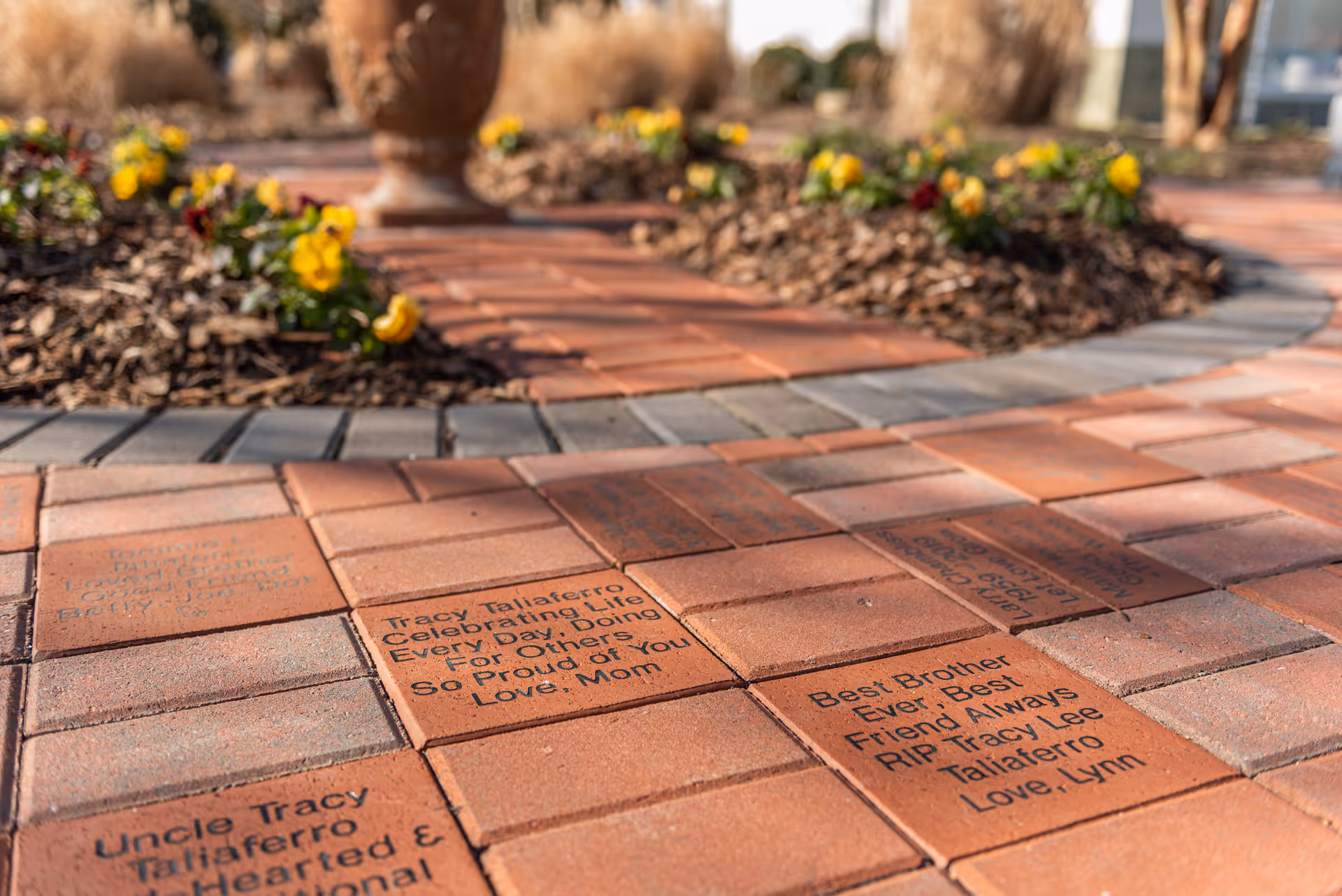 Brick courtyard walkway with engraved memorial bricks and yellow flowers surrounding.