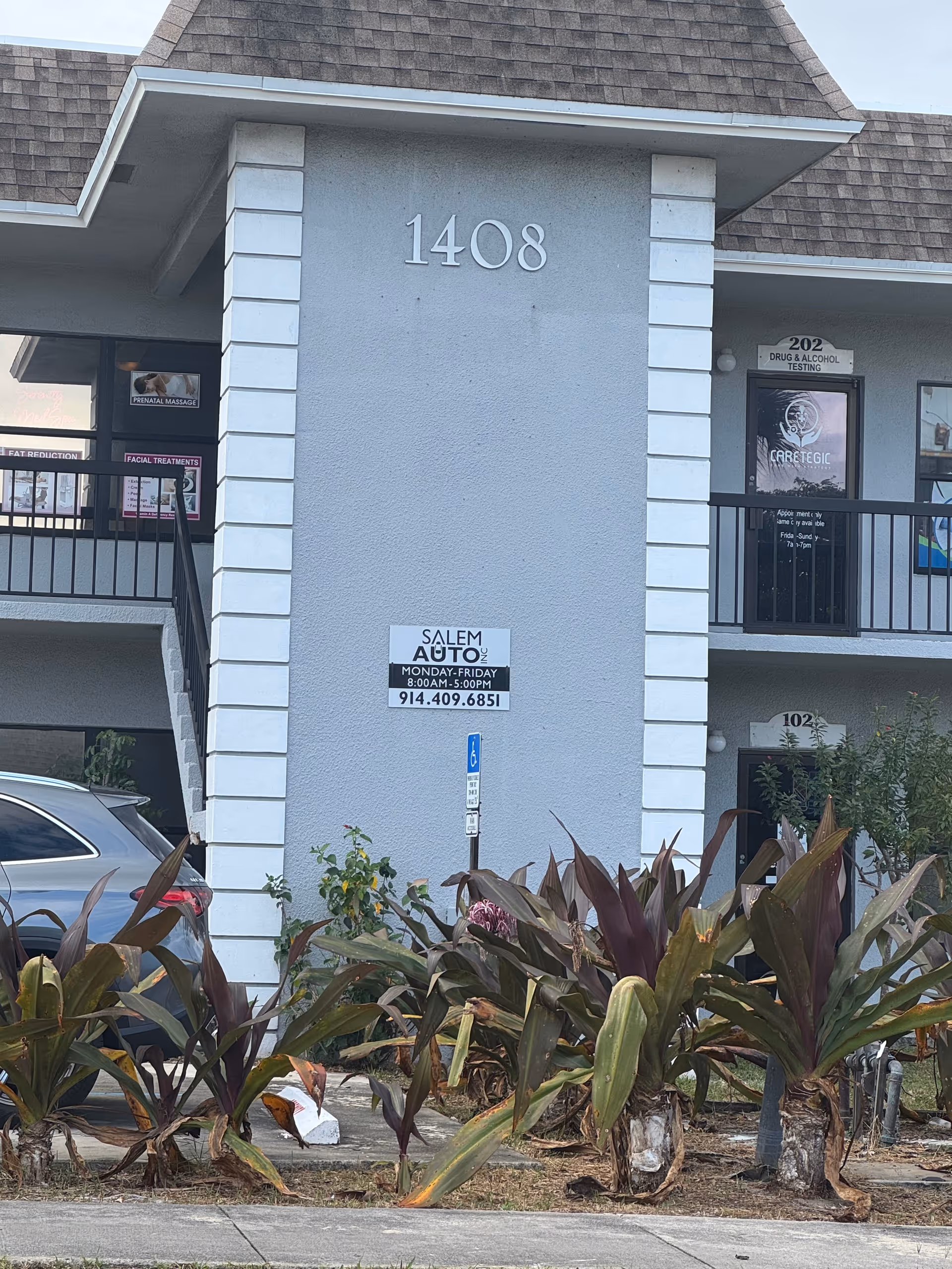 Front of a gray building with the number 1408 and surrounding plants.