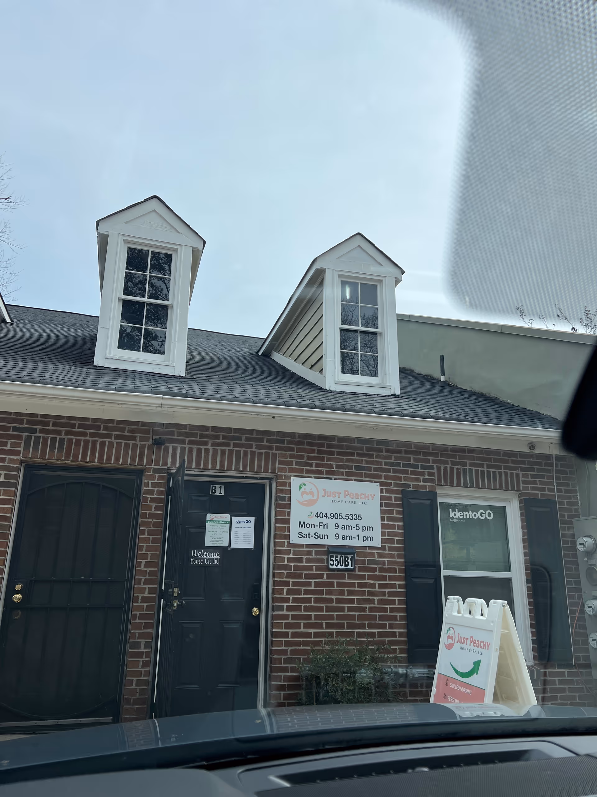 Brick building with two dormer windows, entrance doors, and a Just Peachy Home Care sign.