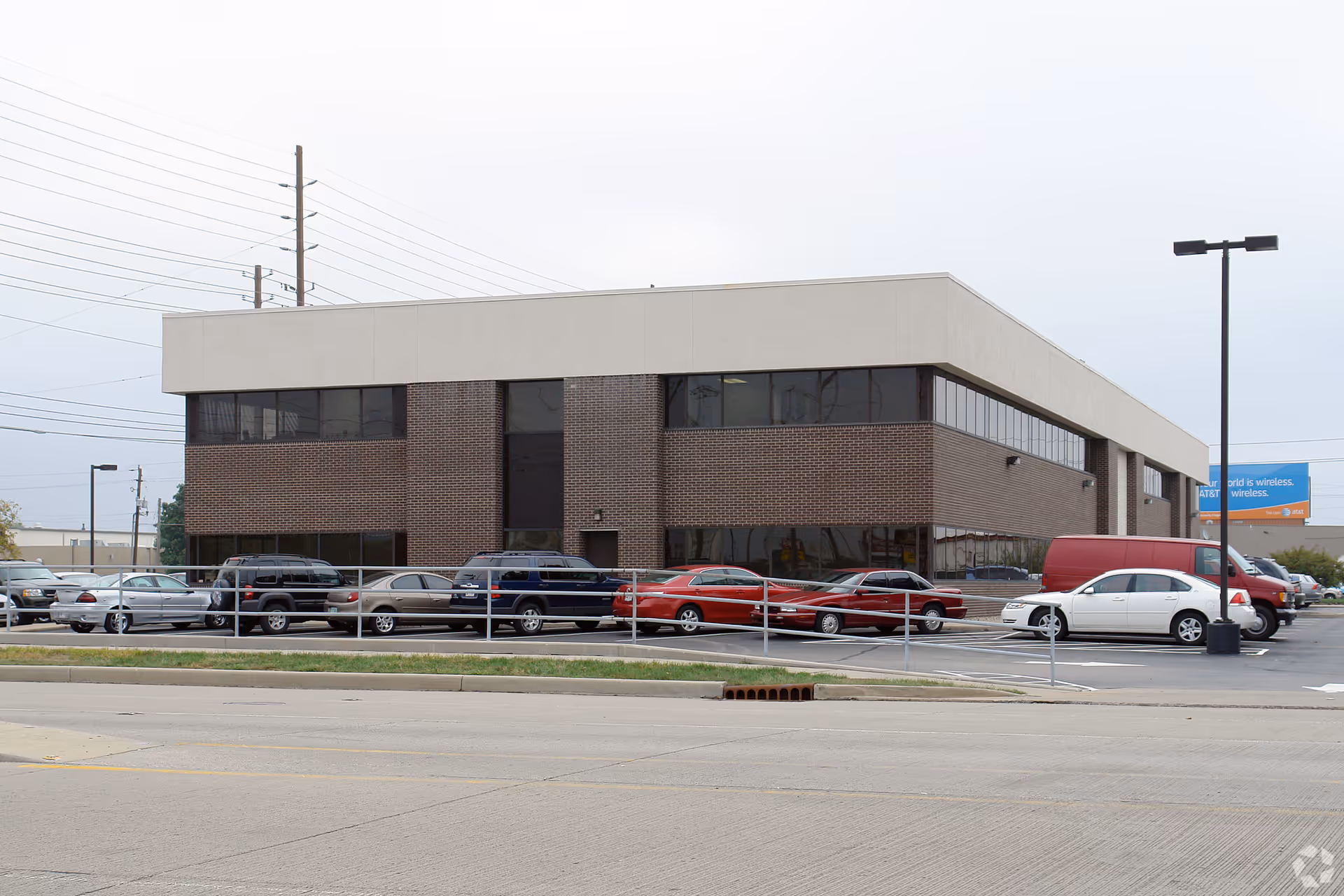 Two-story brick building with a flat, light-colored roof and a parking lot in front.