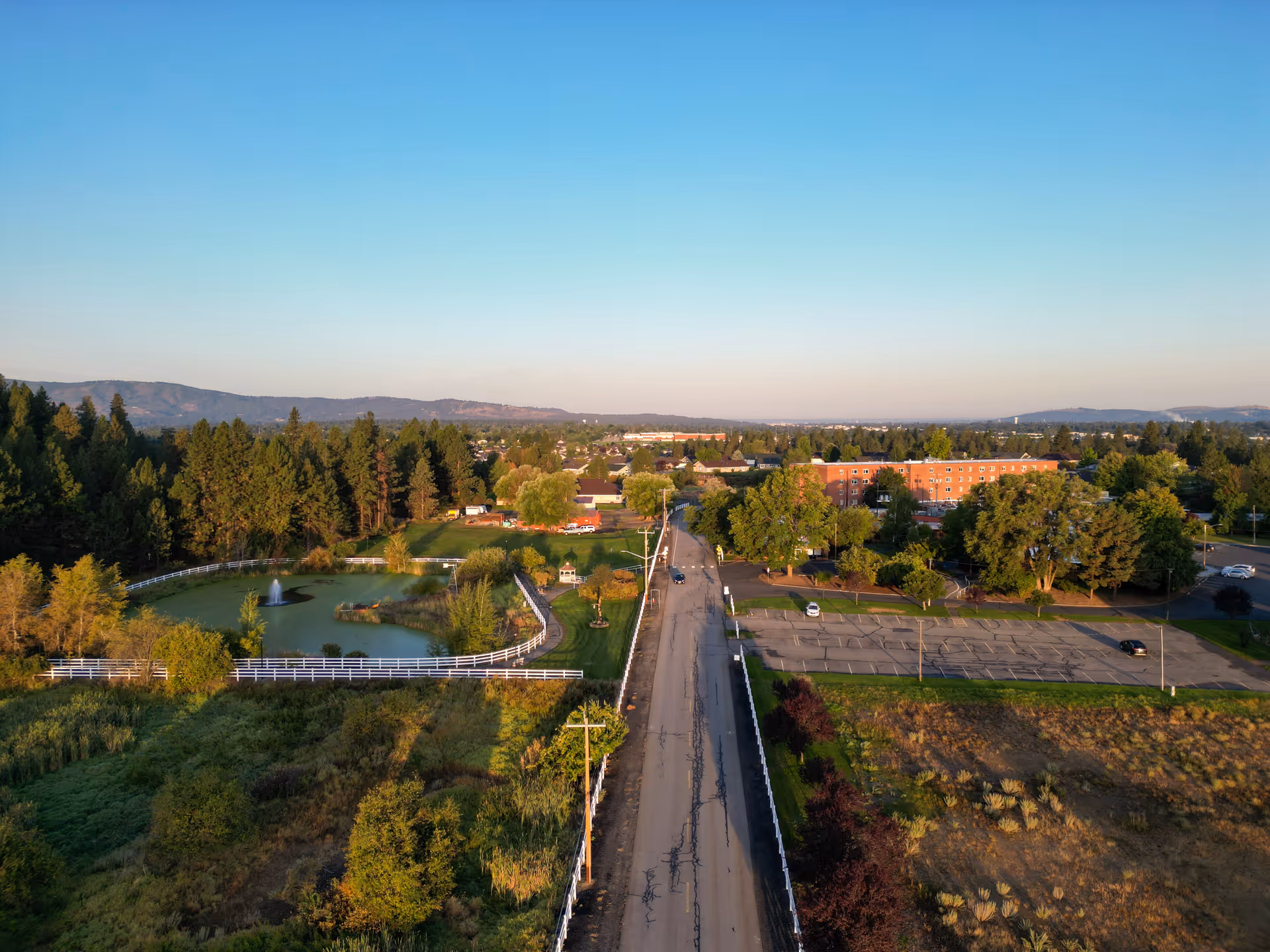 Aerial view of a senior living campus with a road, pond, and trees.