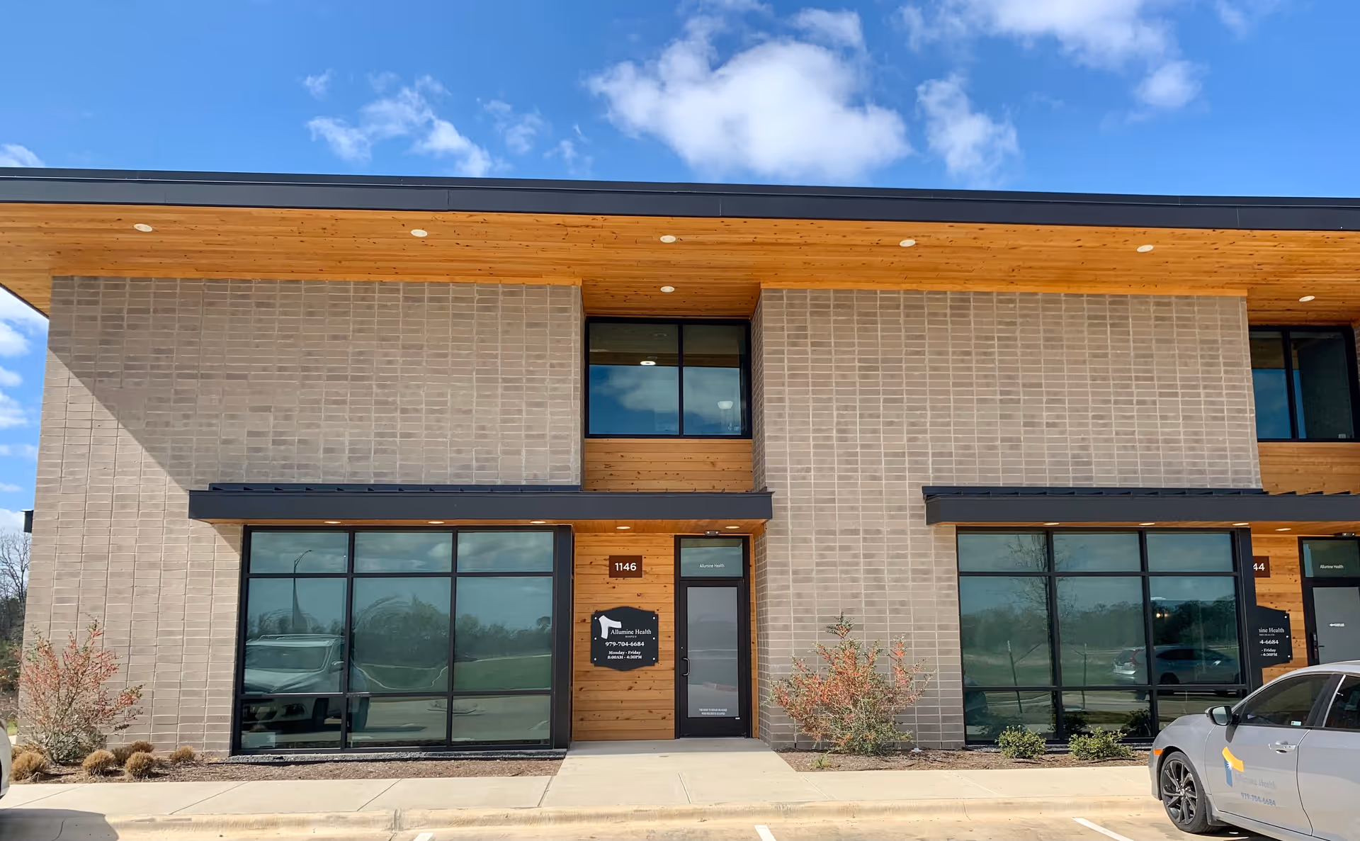 Modern medical facility exterior with brick walls, wooden accents, and large glass storefront windows.