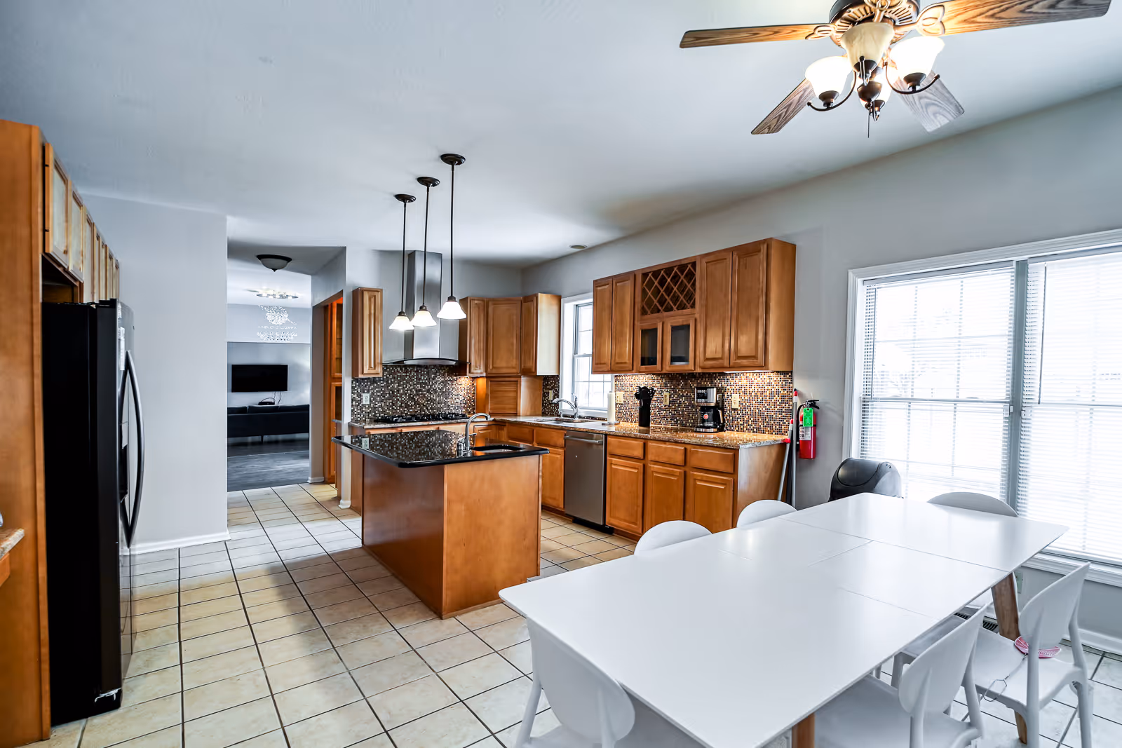 Bright kitchen with island, wooden cabinets, tiled floor, and a white dining table nearby.