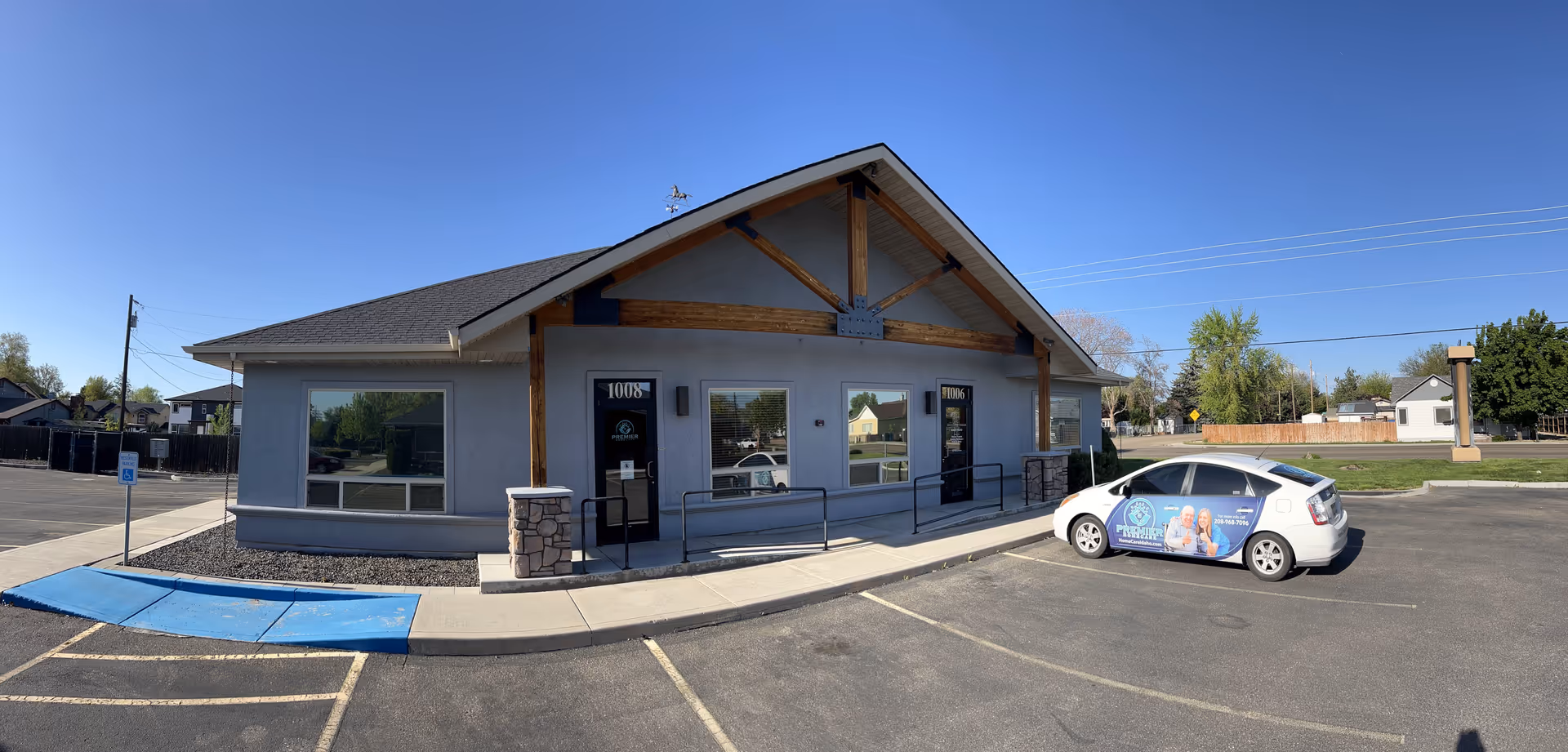 Exterior view of a single-story care facility with a parking lot and a promotional car.