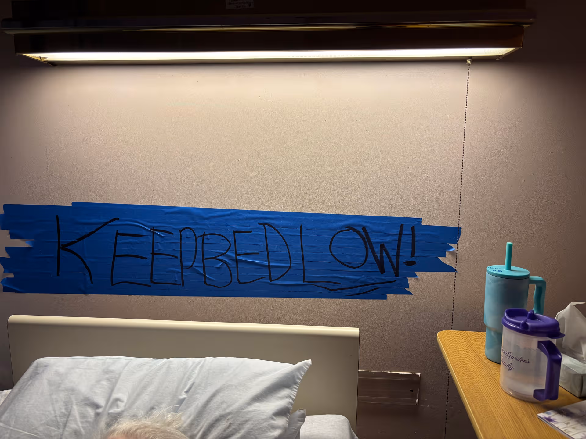 Interior room with a bed and blue taped sign reading KEEP BED LOW.