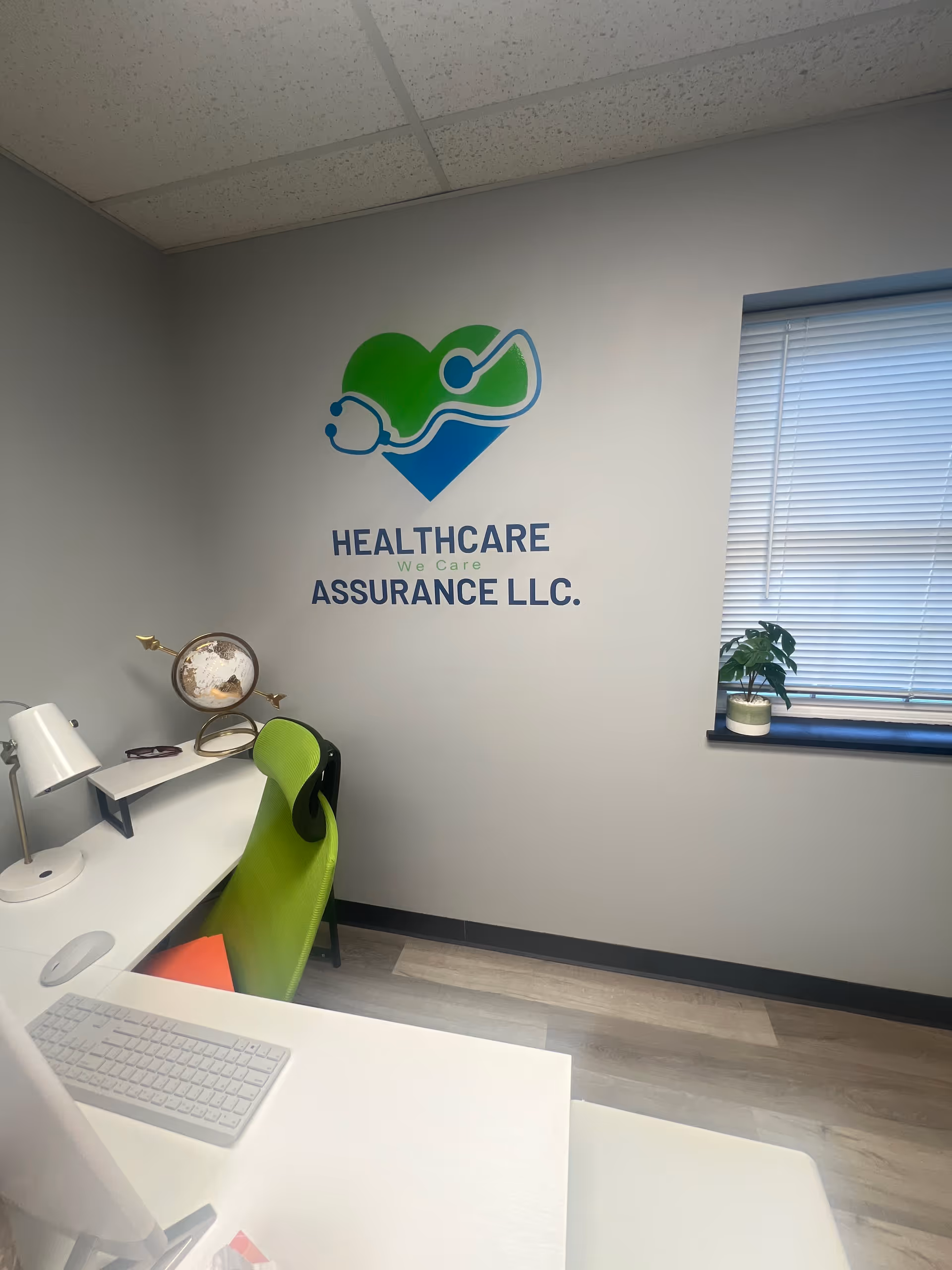 Office desk with white keyboard, lime chair, logo on wall reading Healthcare Assurance LLC, window.