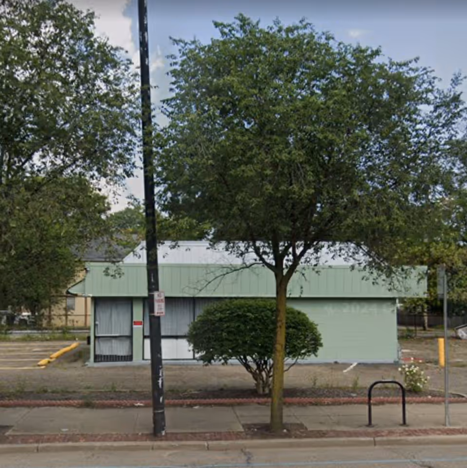 Street view of a pale green building with trees and a sidewalk.