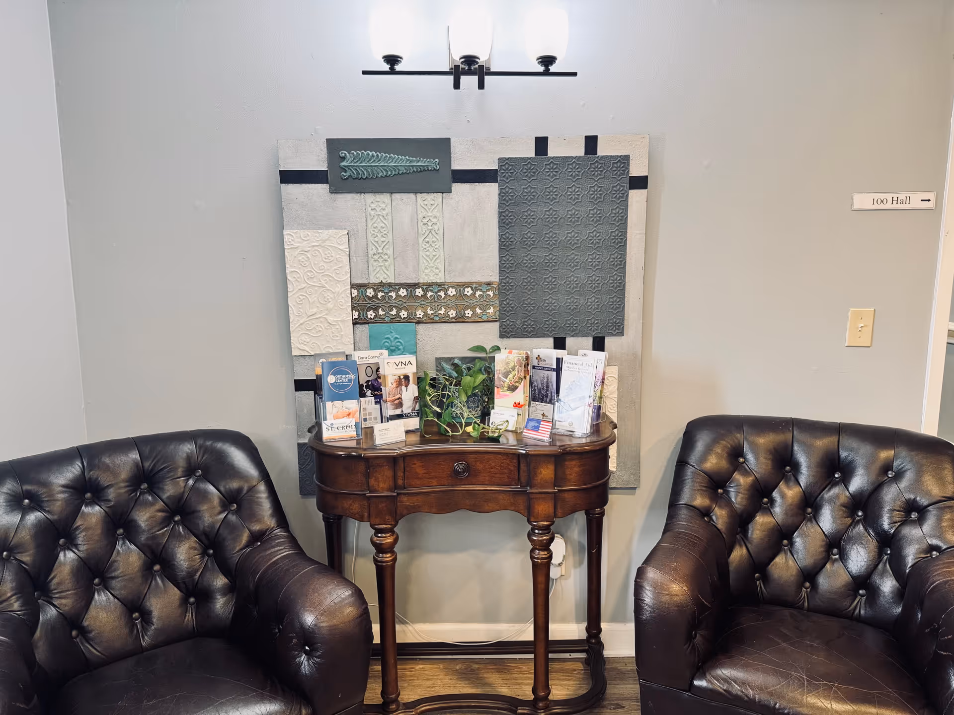 Two black tufted chairs flank a wooden console with brochures in Heritage Village lobby.