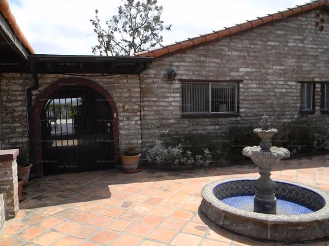Brick building exterior with arched gate, courtyard, potted plants, and a fountain.