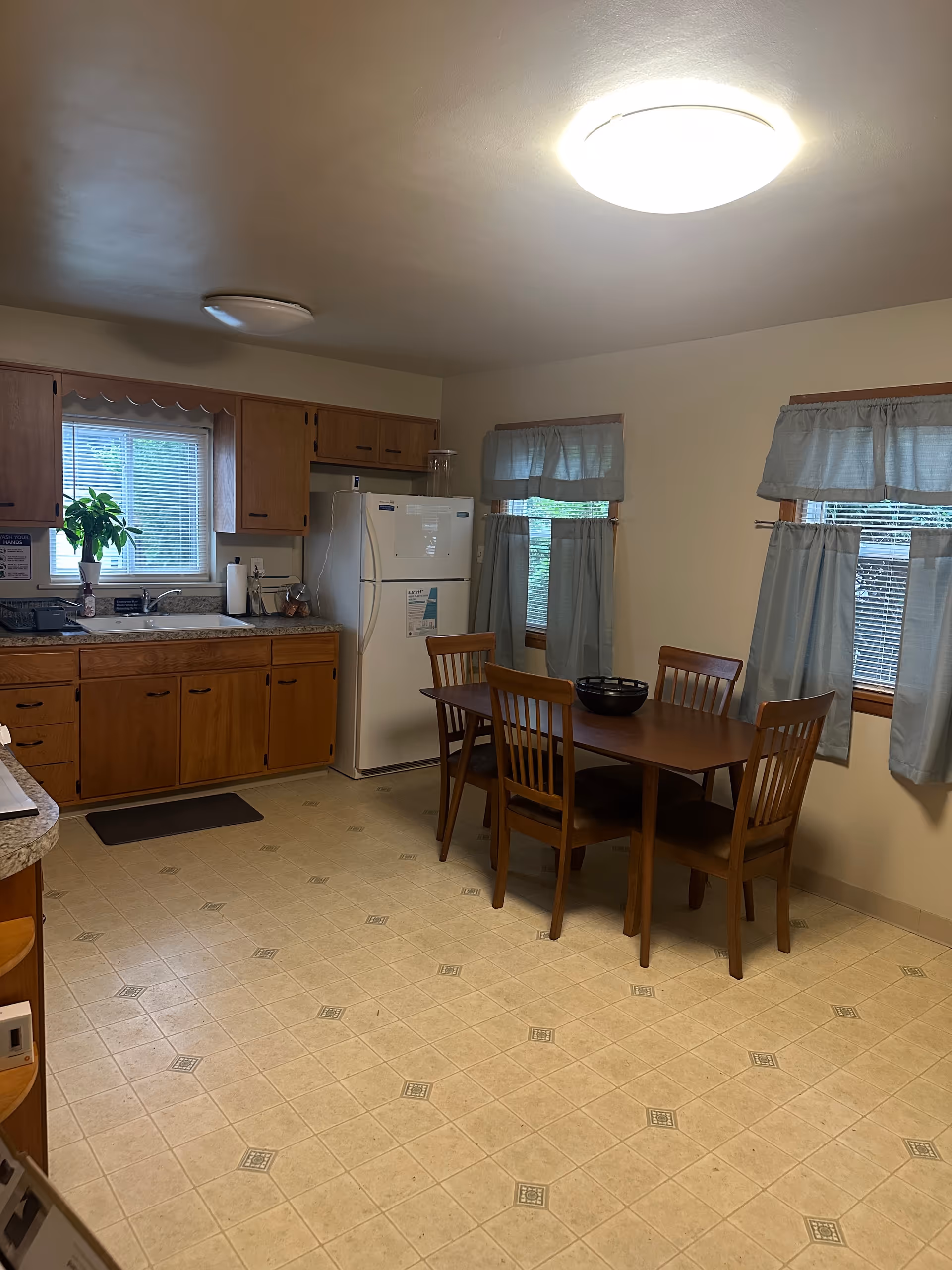 A simple kitchen and dining area with wooden cabinets, a fridge, sink, and table with chairs.