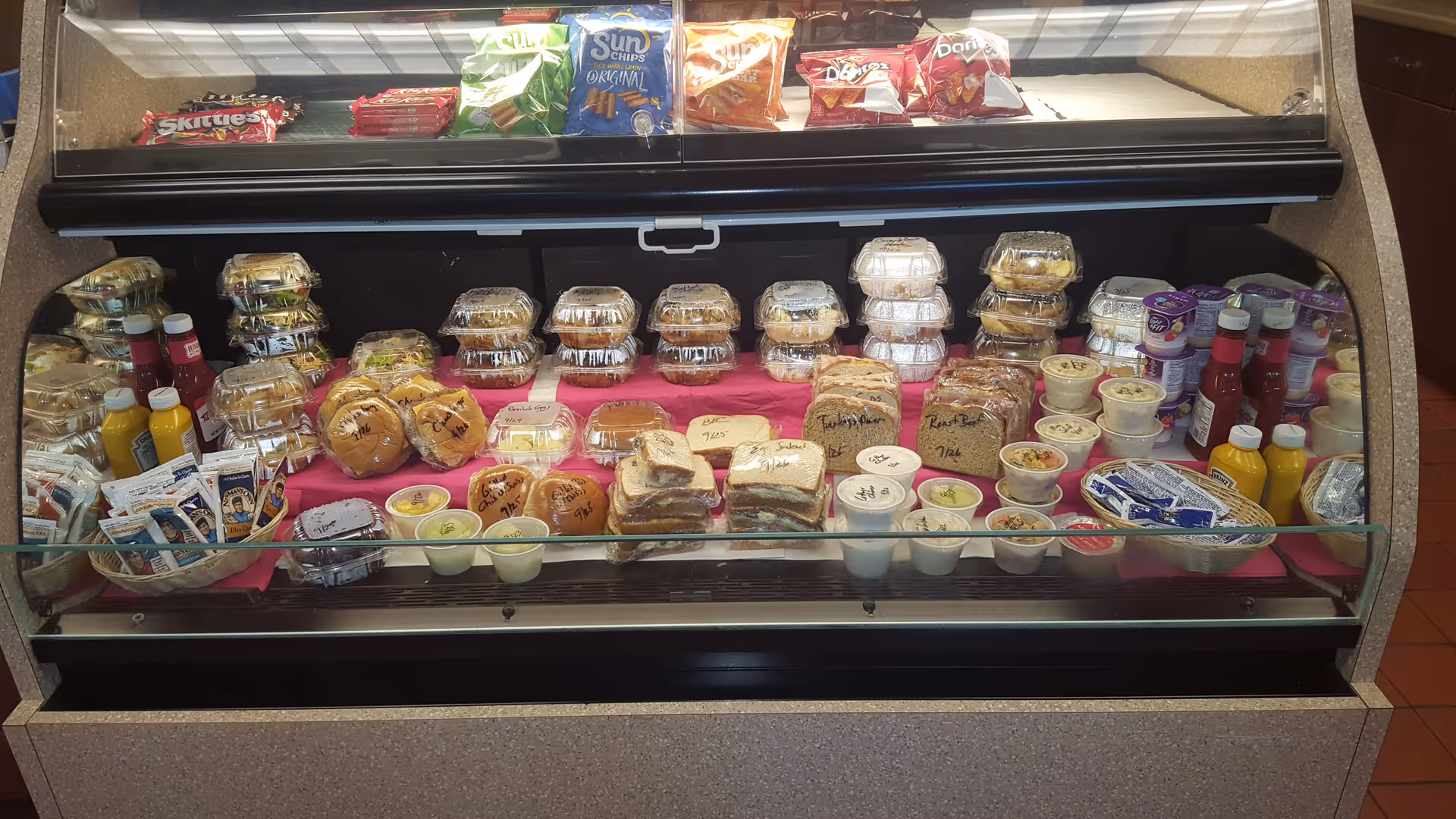 Indoor food display case with pastries, yogurt cups, and juices in a dining area.