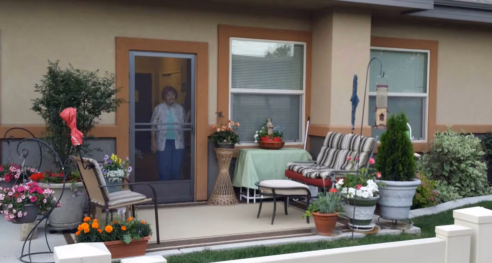 Patio of Grace Assisted Living Meridian with outdoor seating, plants, and a resident by the doorway.