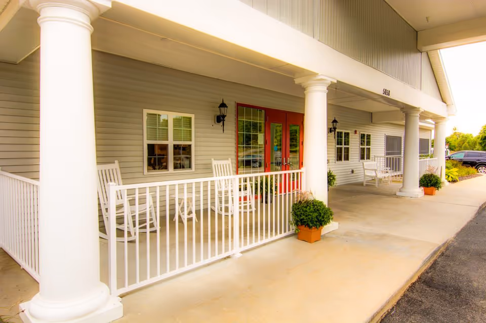 Senior living facility front porch with white rocking chairs and red doors.