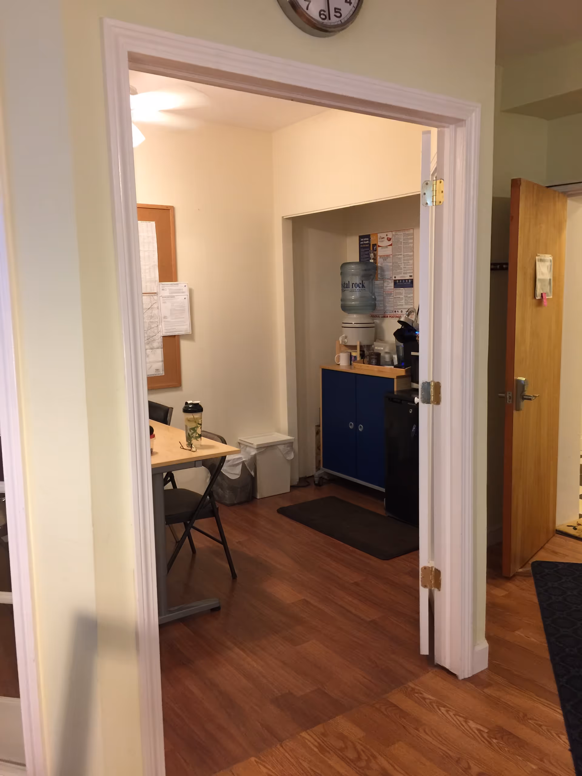 View through doorway of a small staff area with table, water cooler, and blue cabinets.