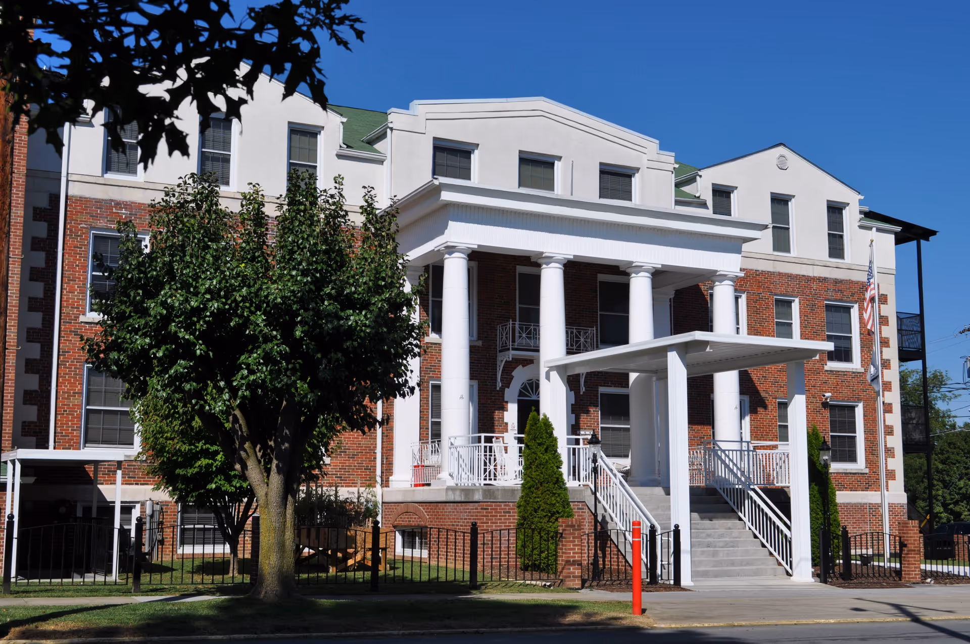 Brick nursing home building front with tall white columns, stairs, and a flag
