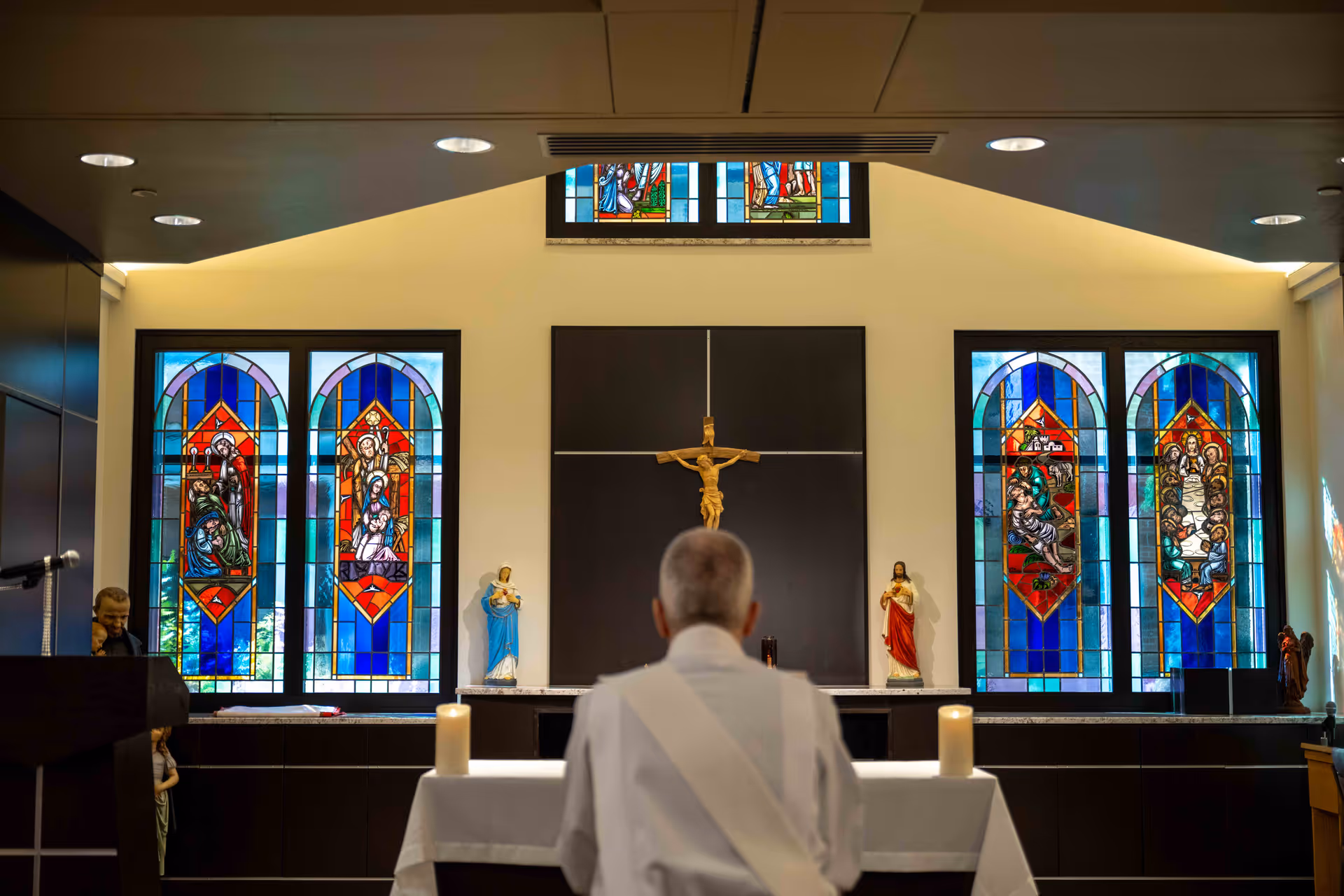 Clergy at the altar inside Rosewood on Broadway chapel with stained-glass windows and crucifix.