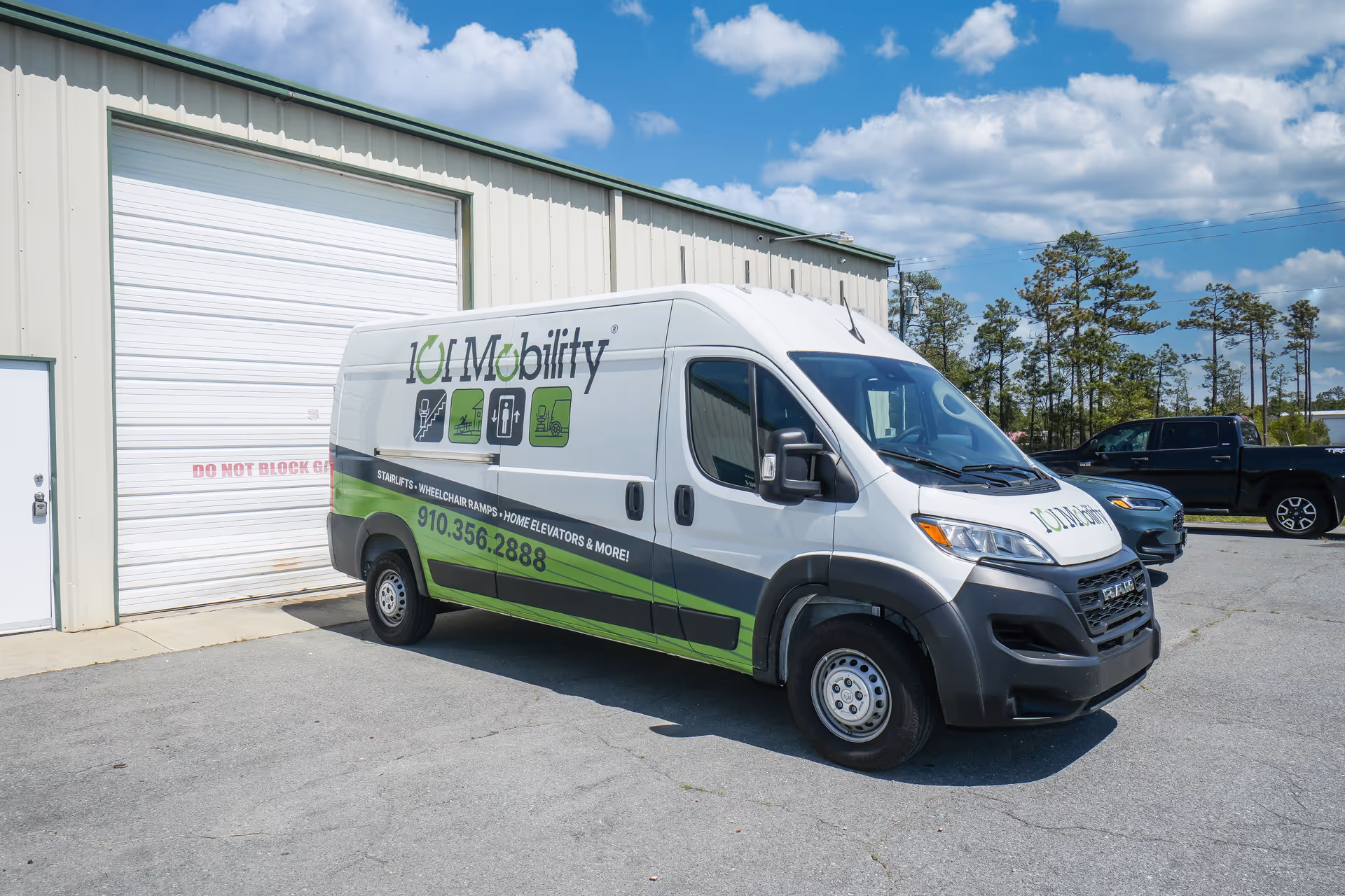 White and green 101 Mobility van parked beside a beige industrial building outdoors.