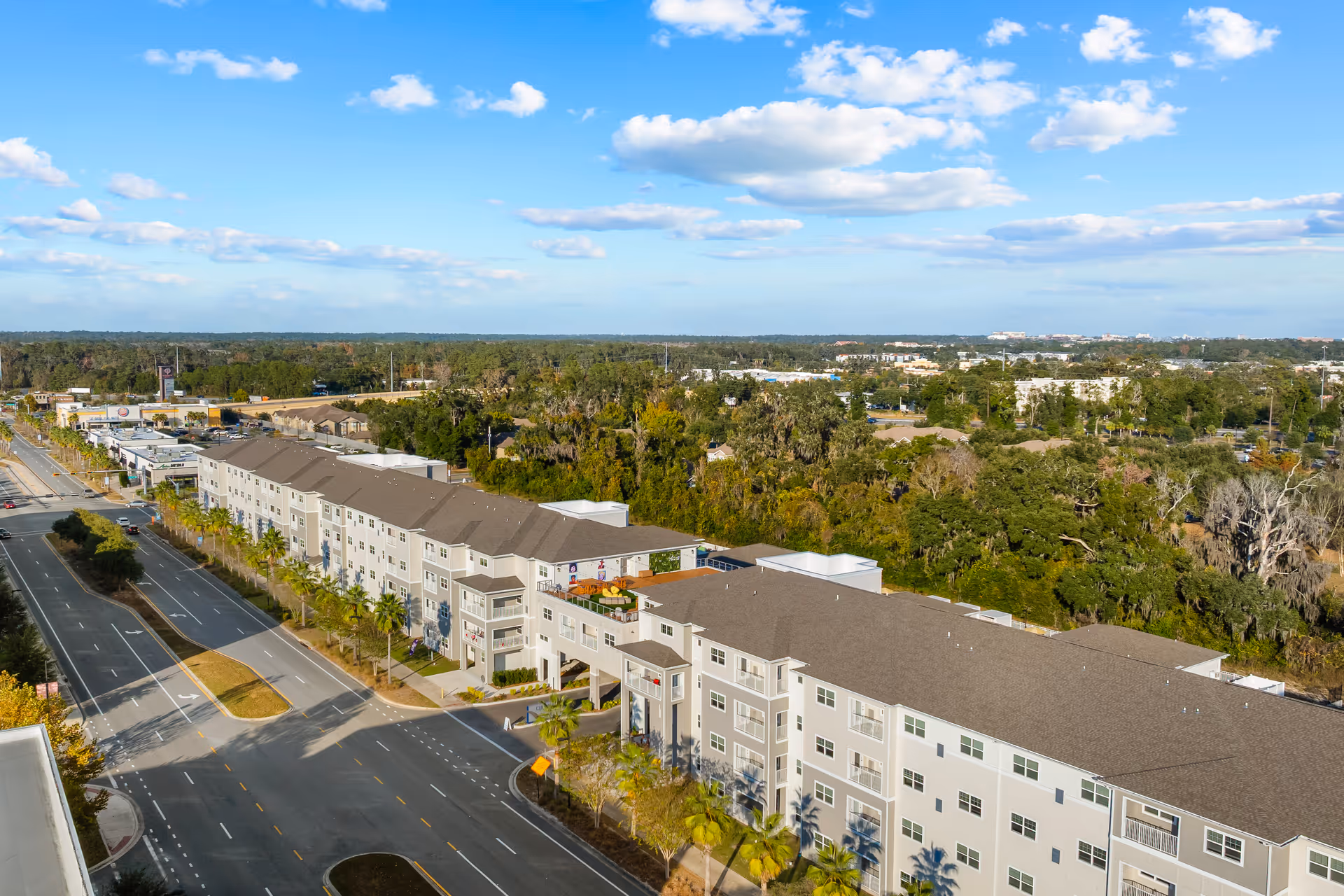 Aerial view of a multi-building senior living campus along a tree-lined street.
