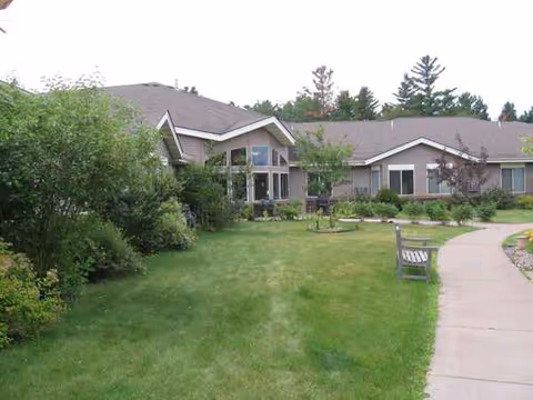 Carlton Place senior living exterior with lawn, walkway, and a bench.