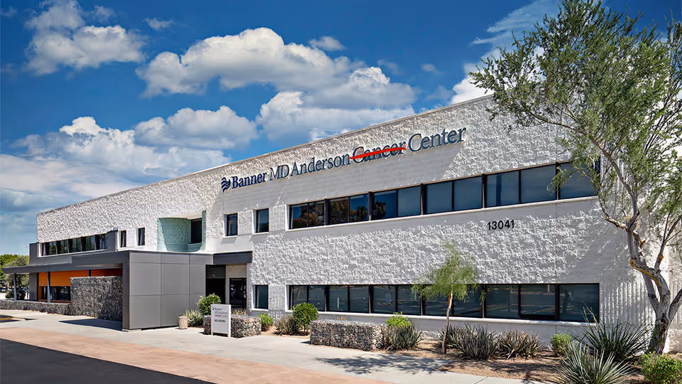White two-story medical center exterior with Banner MD Anderson Cancer Center sign and blue sky.