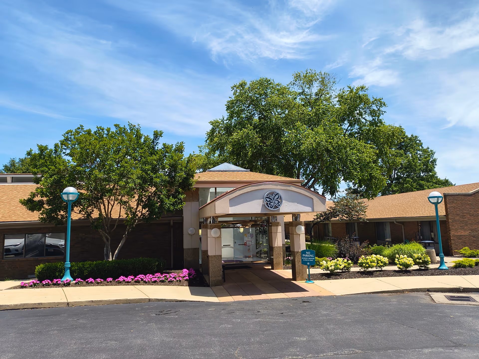 The Delmar Gardens of Overland Park exterior with entrance, trees, and colorful flowers along the walkway.