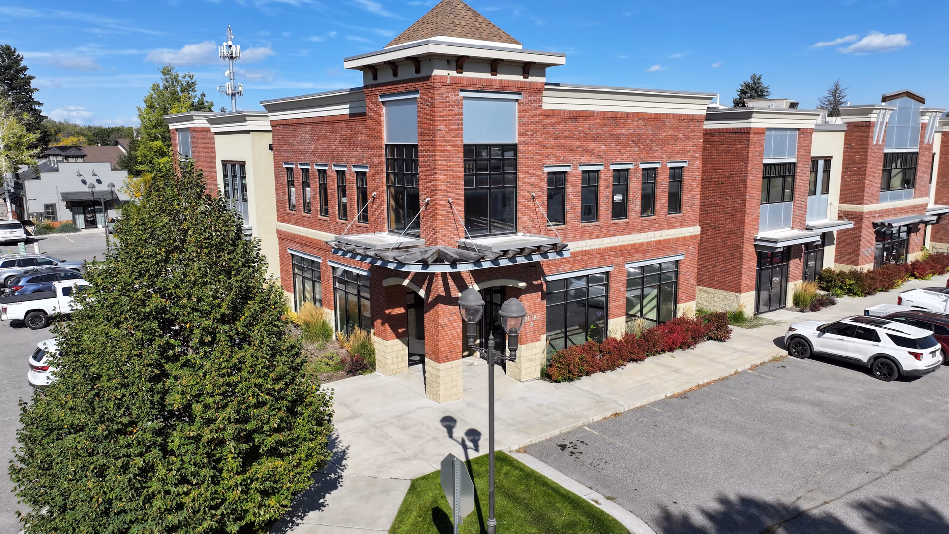 Red brick senior living building with glass entrance, landscaping, and parked cars in a lot.