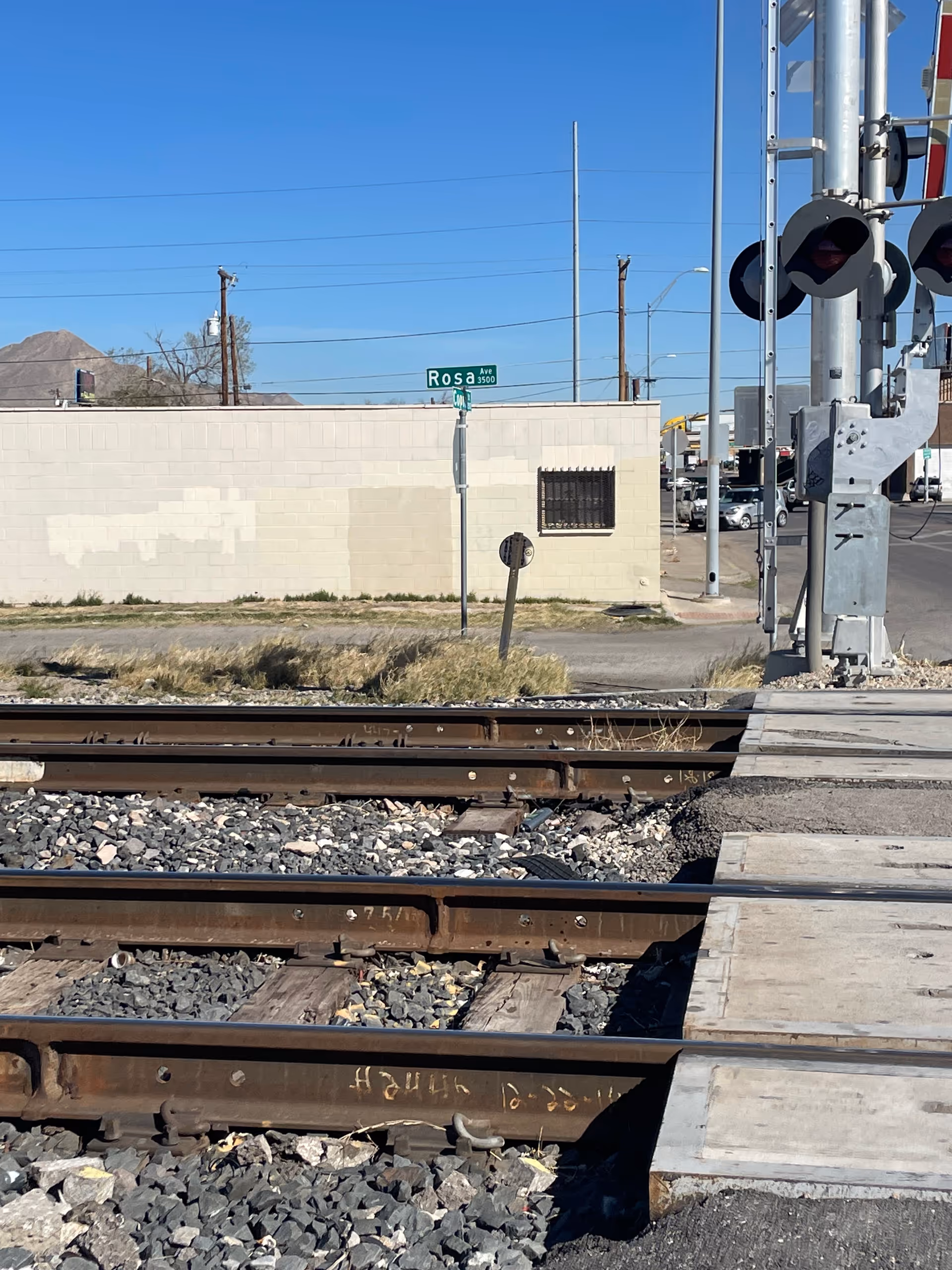 Railroad tracks in the foreground with a beige wall, street sign, and utility poles in view.