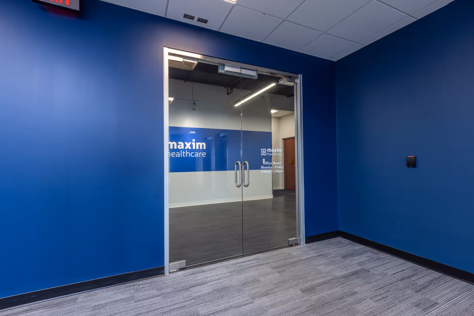 Blue-walled interior corridor with glass doors labeled Maxim Healthcare.