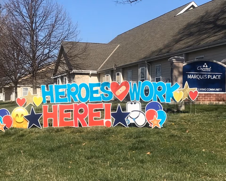 Bright, colorful sign reading HEROES WORK HERE! on a lawn in front of Marquis Place.