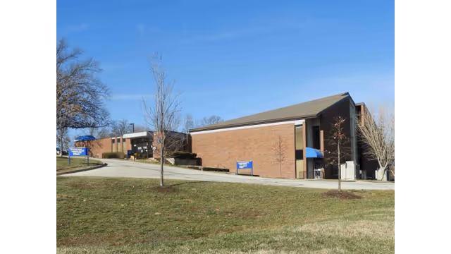 Exterior view of a brick senior living facility with drive, signage, and blue awnings.