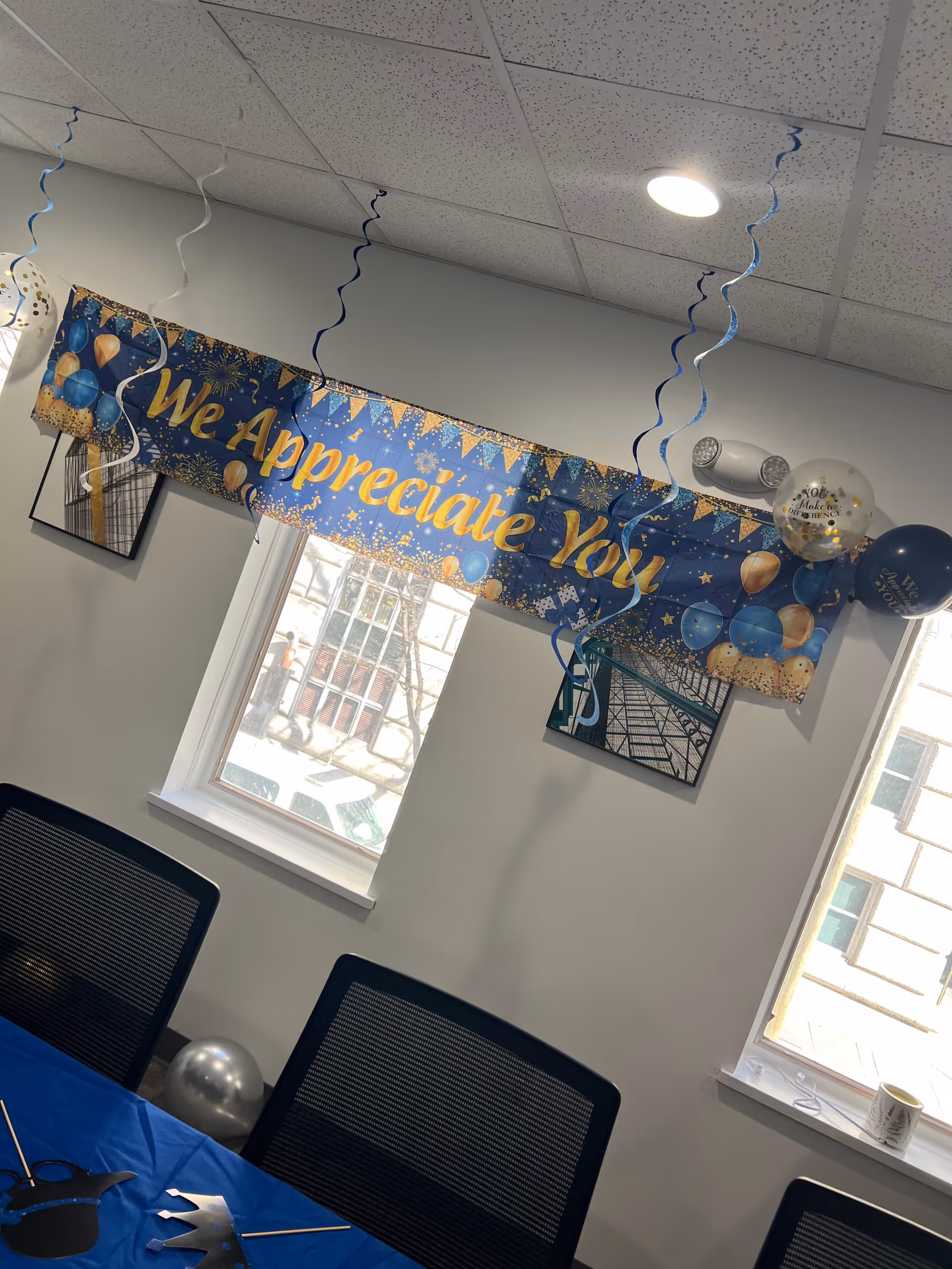Indoor meeting room with a blue 'We Appreciate You' banner and balloons.