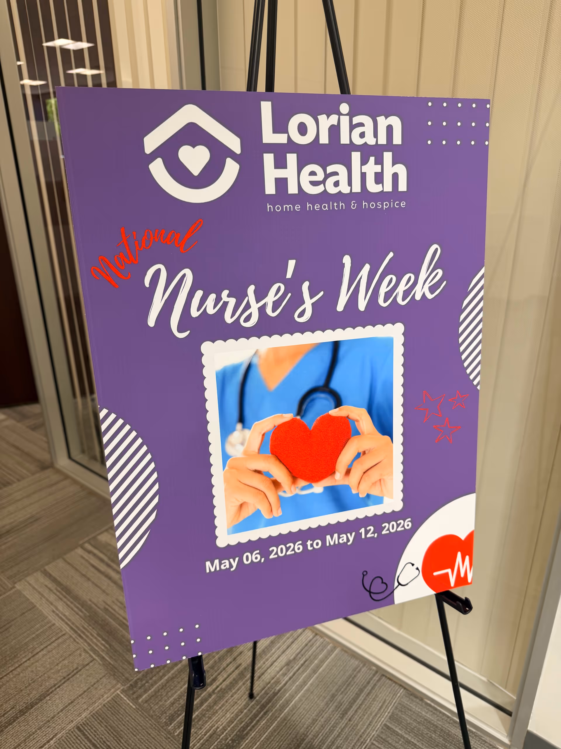 Purple signboard advertising National Nurse's Week at Lorian Health in a hallway.