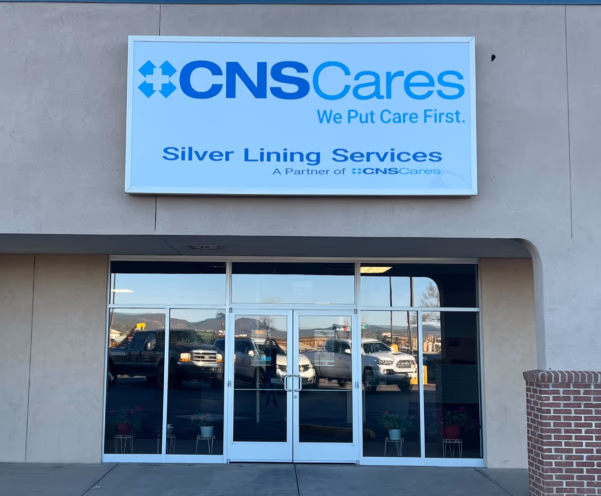 Front exterior of CNS Cares facility shows glass doors and reflected parked cars.