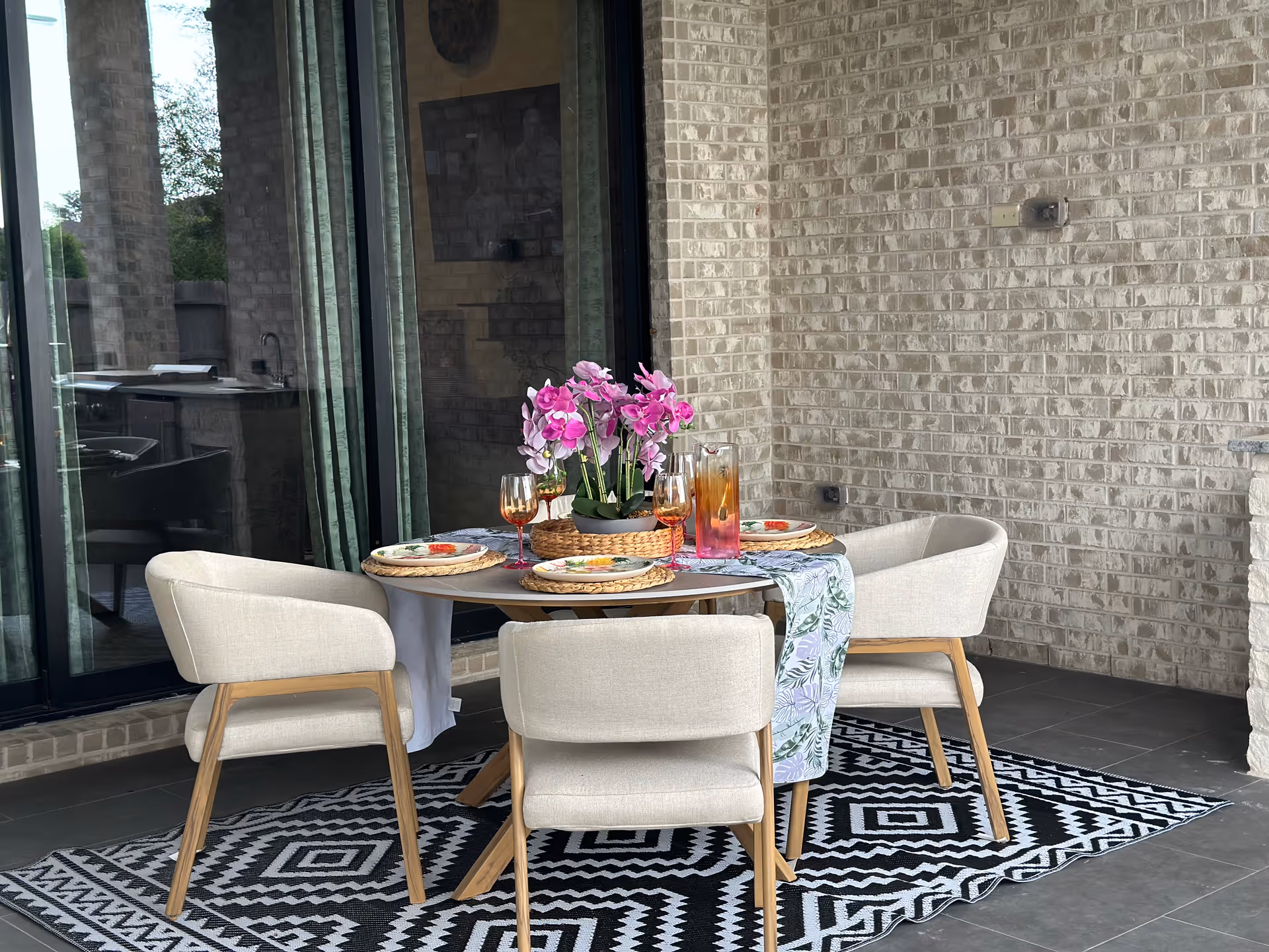 Outdoor patio dining table set with four chairs, plates, drinks, and pink flowers.