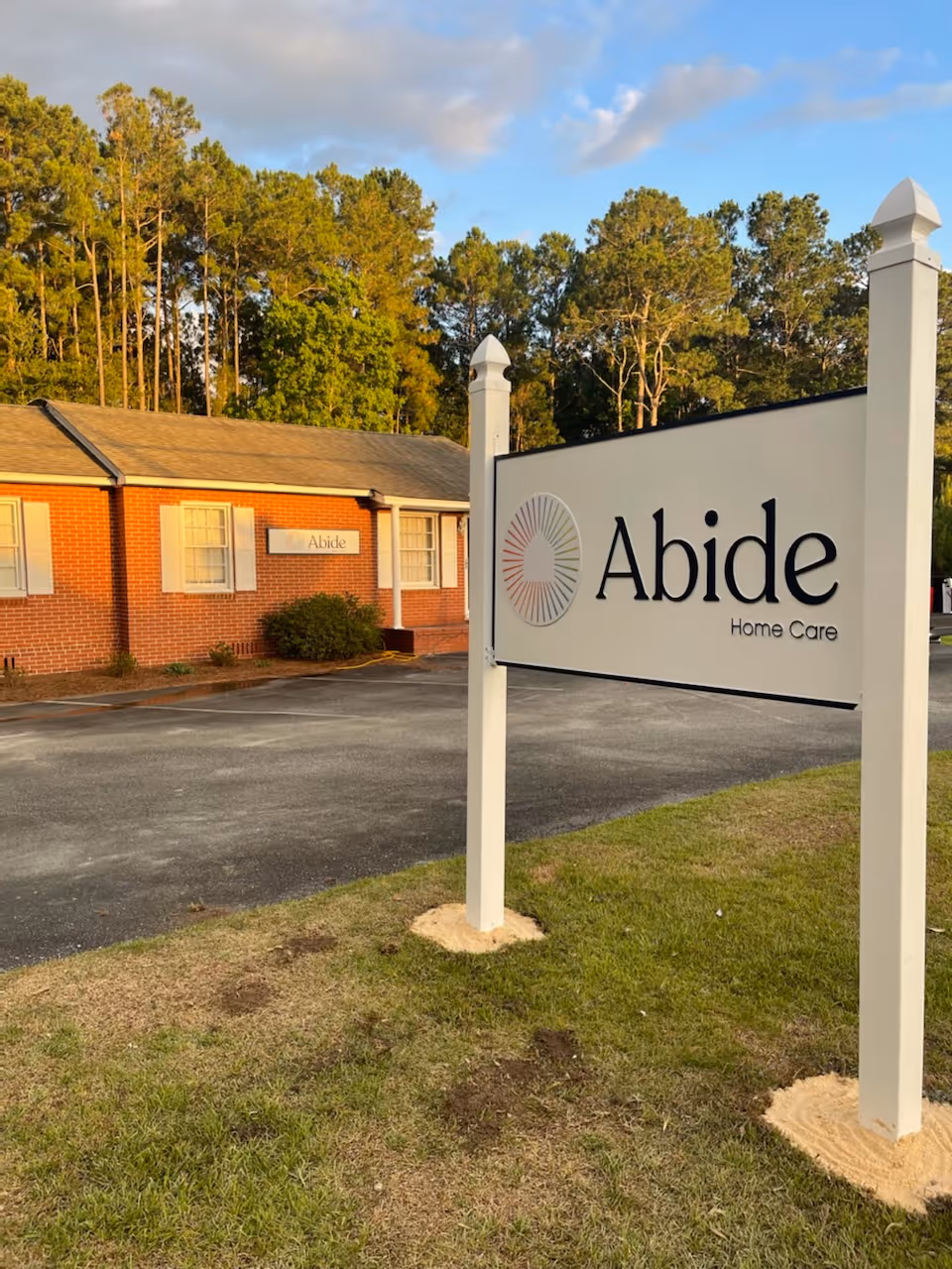 Exterior view of Abide Home Care facility with large sign and brick building in parking lot.