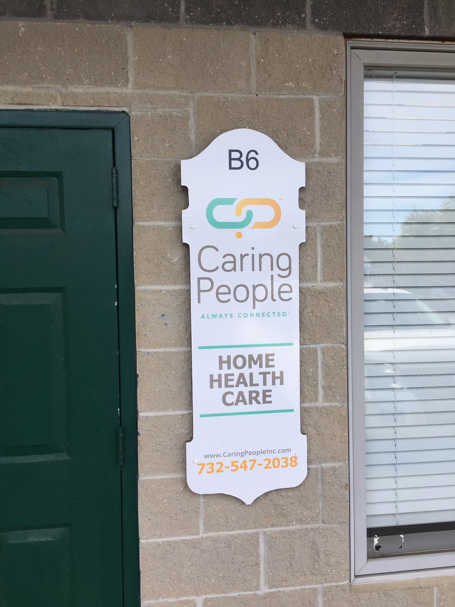 Exterior brick wall with a Caring People home health care sign beside a window.