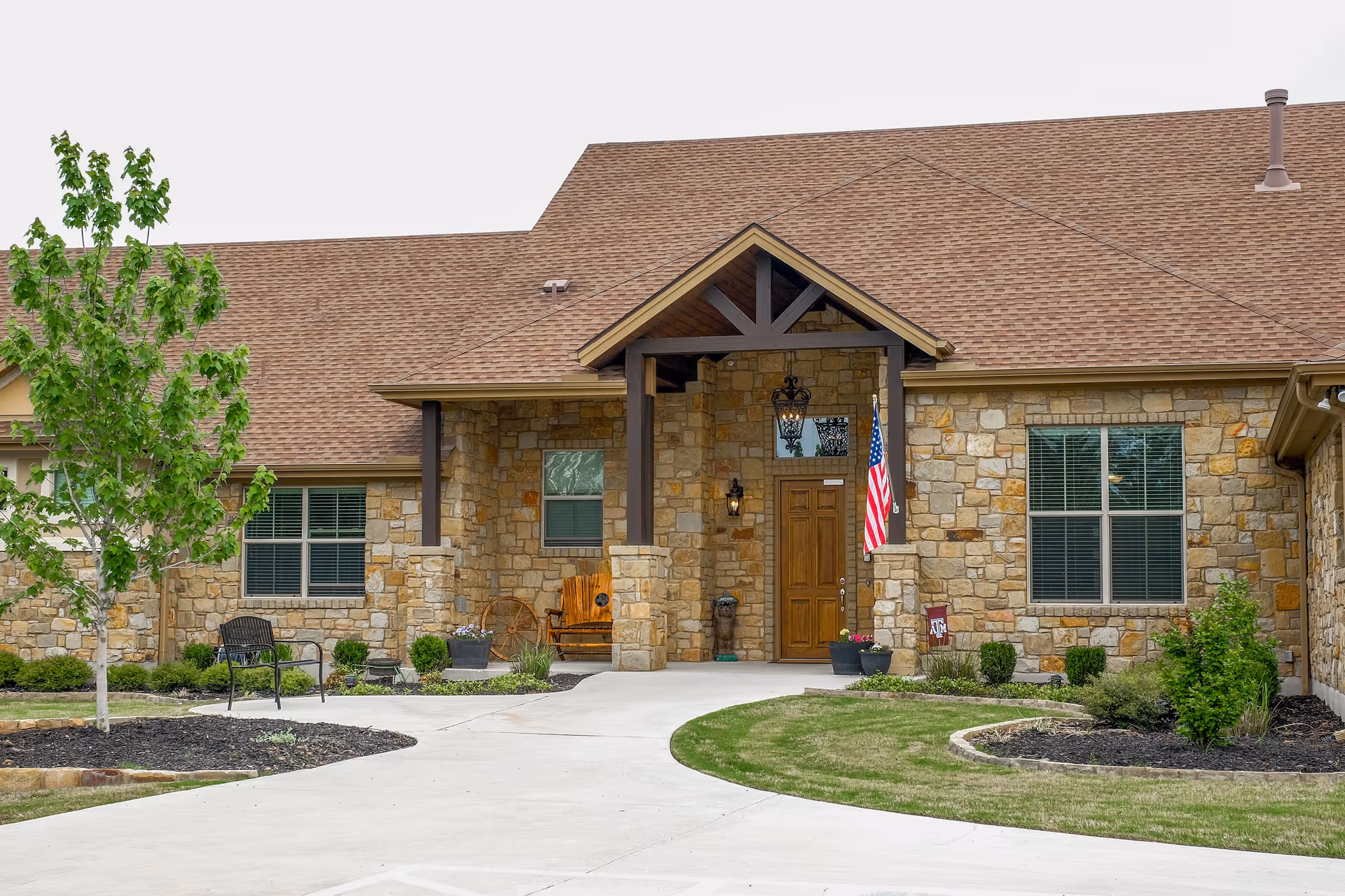 Front view of a stone senior living facility with flag, entryway, and walkway.