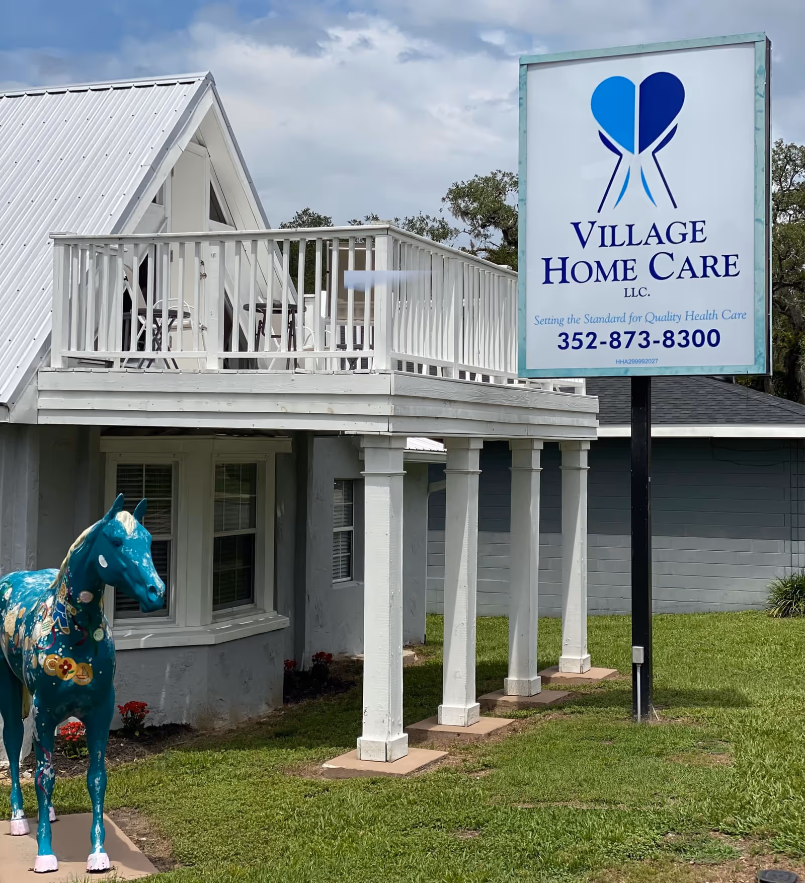 Exterior of Village Home Care facility with a white balcony and blue sign.