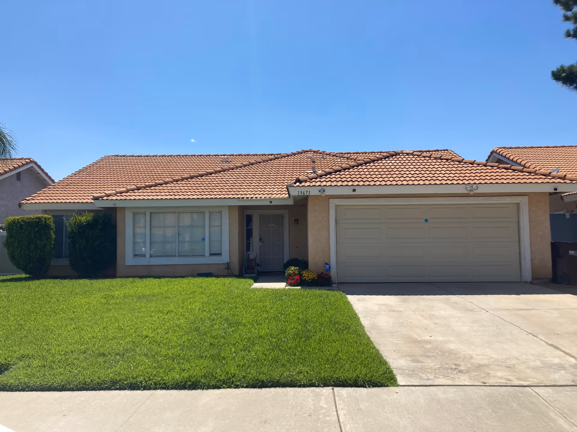 Single-story residential front with beige walls, red tile roof, two-car garage, lawn