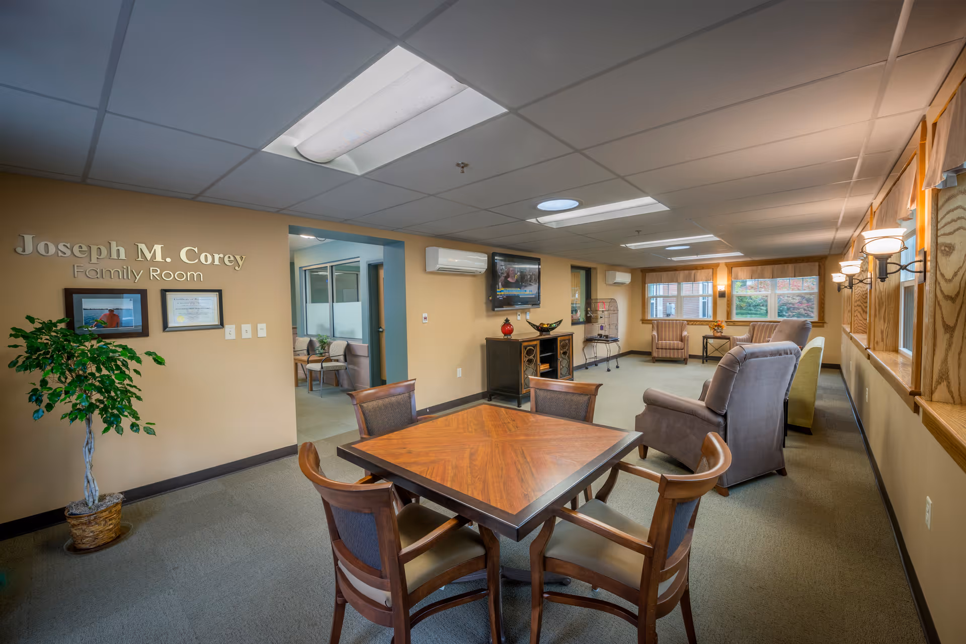 Common living area with square wooden table, chairs, and Joseph M. Corey Family Room sign.