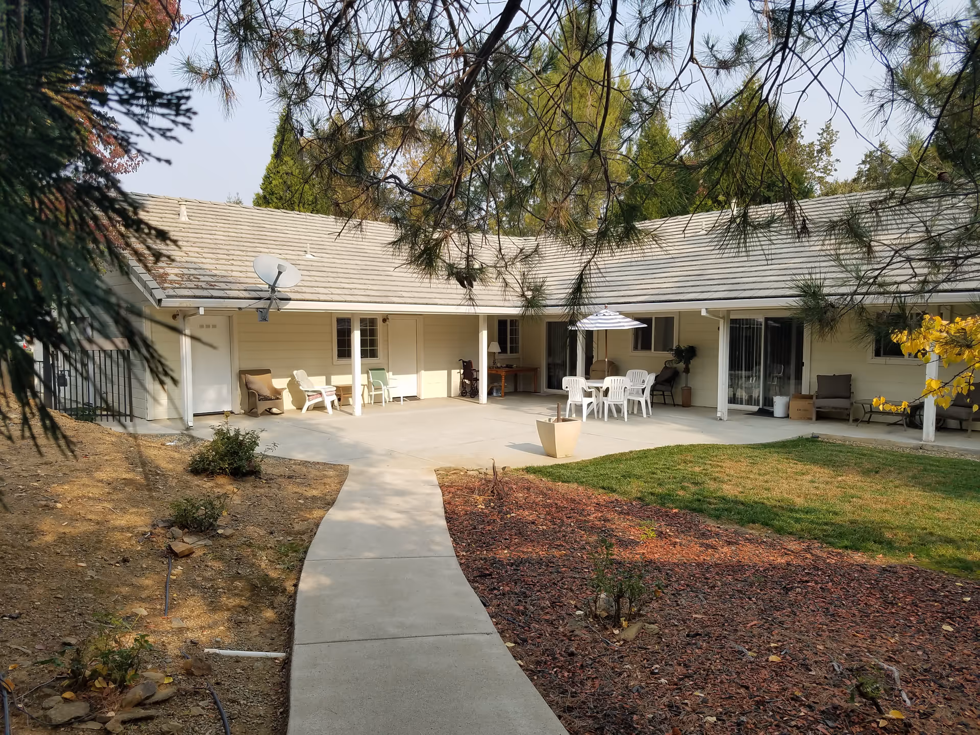 Single-story senior care courtyard with outdoor seating, white chairs, and an umbrella.